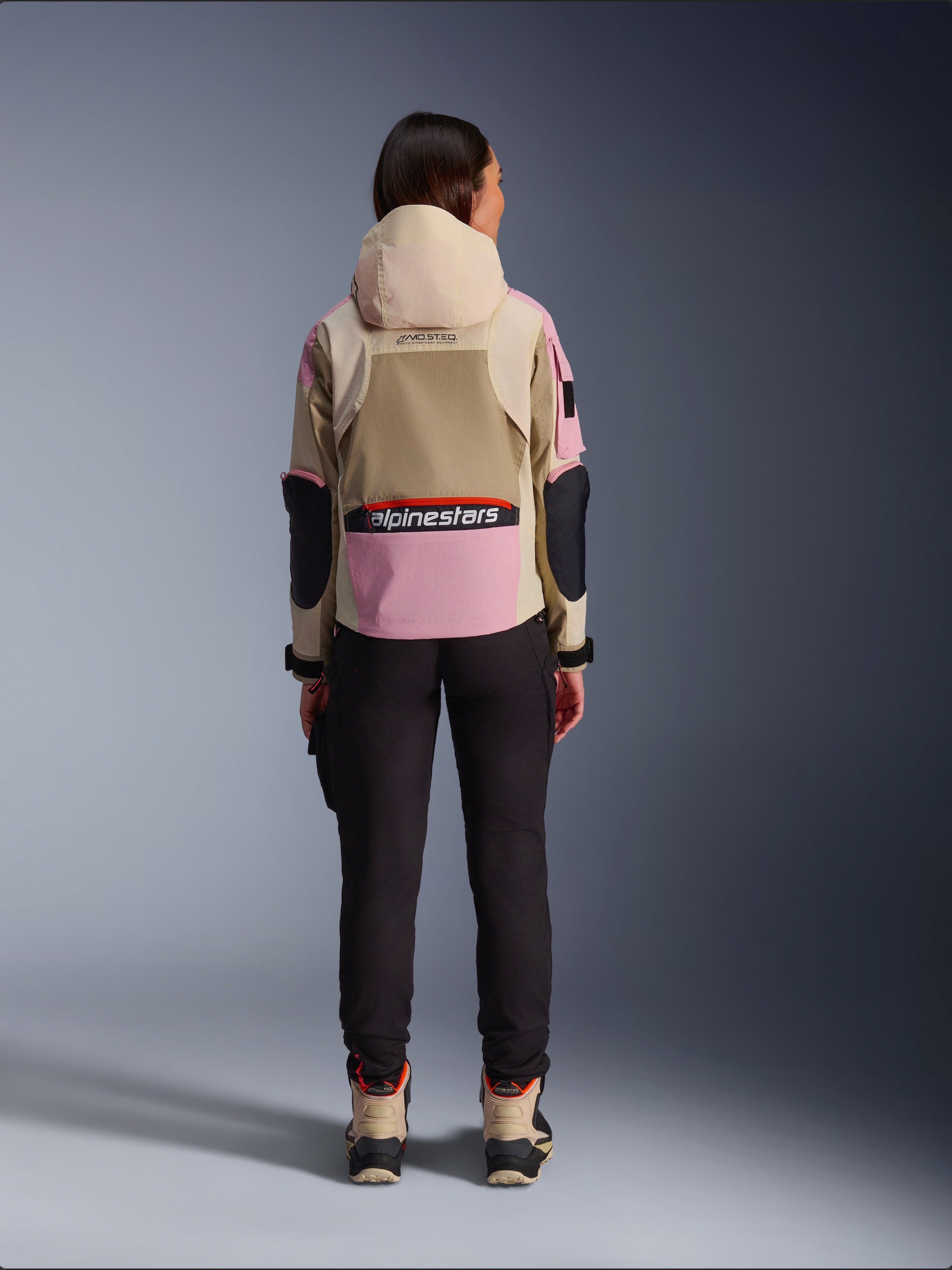 Alpinestars Molly Air Jacket, damska kurtka motocyklowa widziana od tyłu, kolor Sand Pink Almond, beżowy kaptur i różowe panele z czarnymi akcentami, czarne spodnie i beżowe buty motocyklowe, współczesna miejska odzież motocyklowa