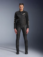 Modelka w damskiej kurtce motocyklowej Alpinestars Stella T-Dyno Air w kolorze czarnym, z panelami z siatki 3D i białym logo Astars, zestawiona z czarnymi dopasowanymi spodniami motocyklowymi i czarnymi sznurowanymi butami, styl miejskiej odzieży motocyklowej.