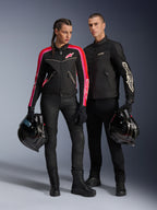 Mężczyzna i kobieta pozujący w odzieży motocyklowej Alpinestars, mężczyzna w czarnej kurtce T-Dyno Air Jacket, kobieta w czarnej kurtce tekstylnej z różowymi i czerwonymi akcentami, oboje trzymają czarne kaski integralne, stylizacja z czarnymi spodniami i butami motocyklowymi.