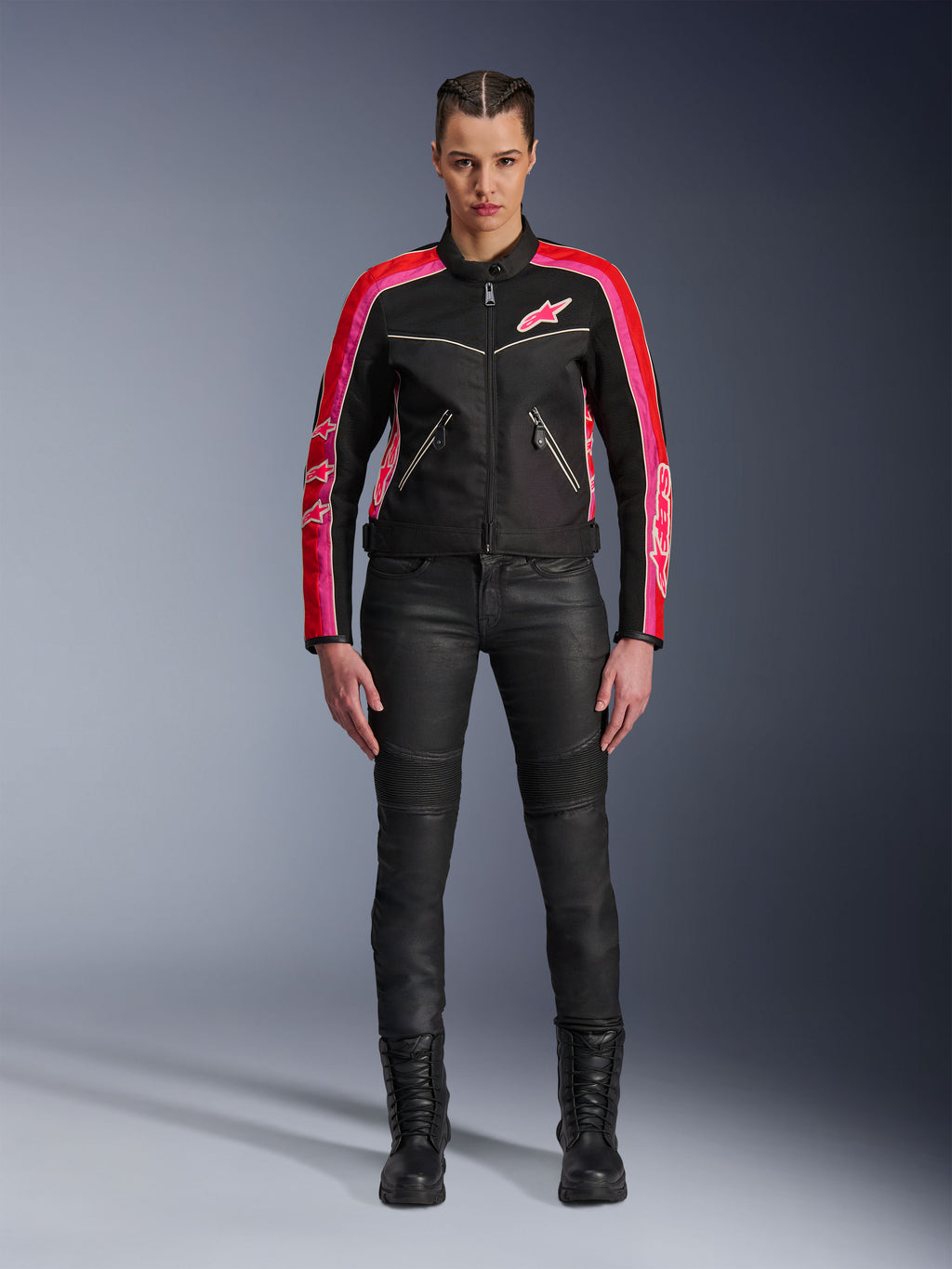Motocyklistka w kurtce Alpinestars Stella T-Dyno Air, czarna z jaskrawoczerwonymi i fuksjowymi akcentami, zestawiona z czarnymi spodniami motocyklowymi i sznurowanymi butami, panele z siatki 3D, dopasowany krój, różowe logo gwiazdy, miejski strój motocyklowy