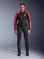 Motocyklistka w kurtce Alpinestars Stella T-Dyno Air, czarna z jaskrawoczerwonymi i fuksjowymi akcentami, zestawiona z czarnymi spodniami motocyklowymi i sznurowanymi butami, panele z siatki 3D, dopasowany krój, różowe logo gwiazdy, miejski strój motocyklowy