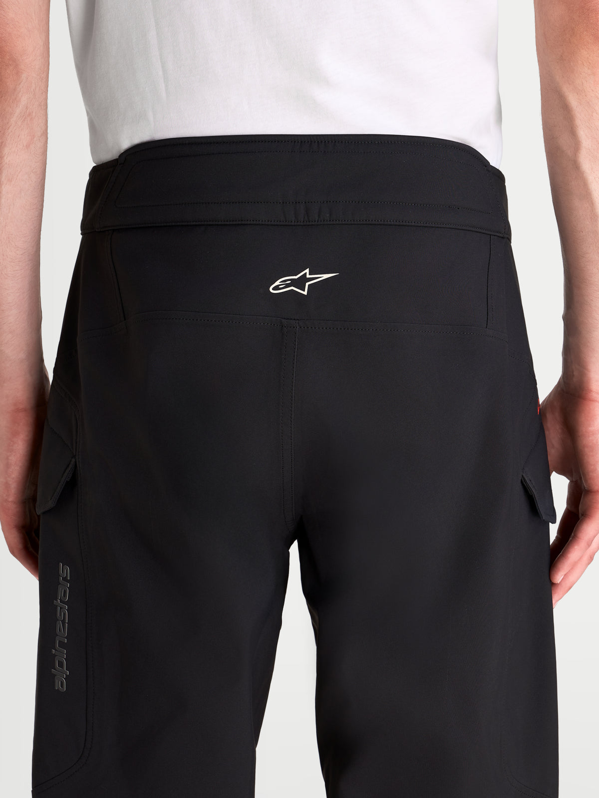 Alpinestars Juggernaut V2 Drystar spodnie motocyklowe miejskie męskie, czarne, widok z tyłu na wysoki pas, ergonomiczny tył, białe logo Alpinestars i boczne kieszenie typu cargo noszone przez model