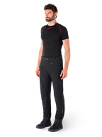 Alpinestars Alden Pants, miejskie spodnie motocyklowe, czarne, tekstylny softshell o regularnym kroju, prezentowane na modelu z czarną warstwą bazową i butami do jazdy, wyposażone w pasek w talii z zapięciem magnetycznym i kieszenie na zamek.