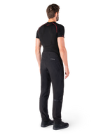 Alpinestars Alden Pants, czarne, miejskie spodnie motocyklowe widoczne od tyłu na modelu, noszone z czarną koszulką z krótkim rękawem i czarnymi butami do jazdy, z pikowanymi detalami i odblaskowym logo MO.ST.EQ. na tylnym karczku.