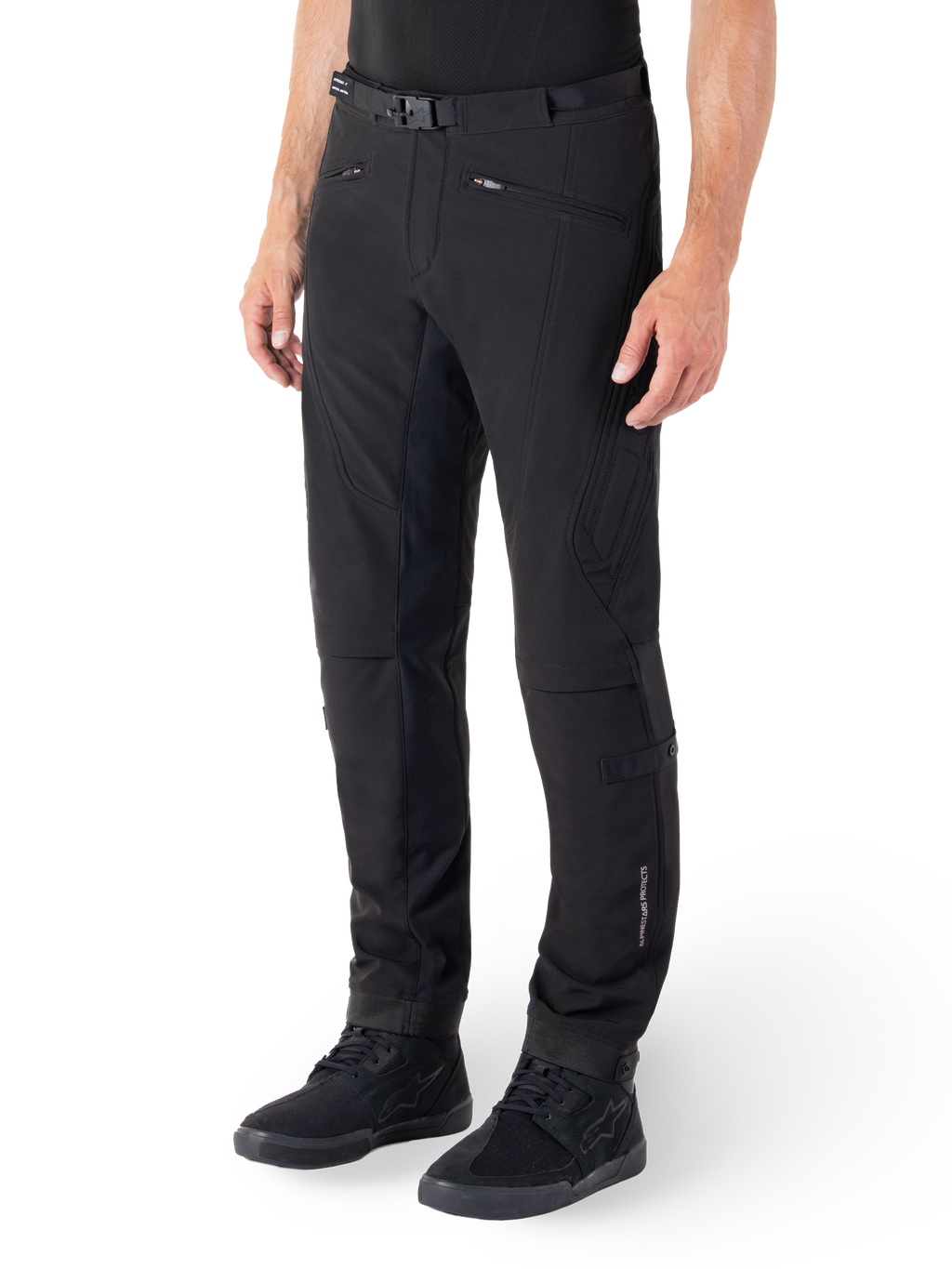 Alpinestars Alden Pants, miejskie spodnie motocyklowe, czarne, techniczna tkanina softshell o regularnym kroju, magnetyczna klamra w pasie, pikowane panele boczne, kieszenie na zamek i subtelne logo na dolnej części nogawki, noszone z czarnymi butami motocyklowymi