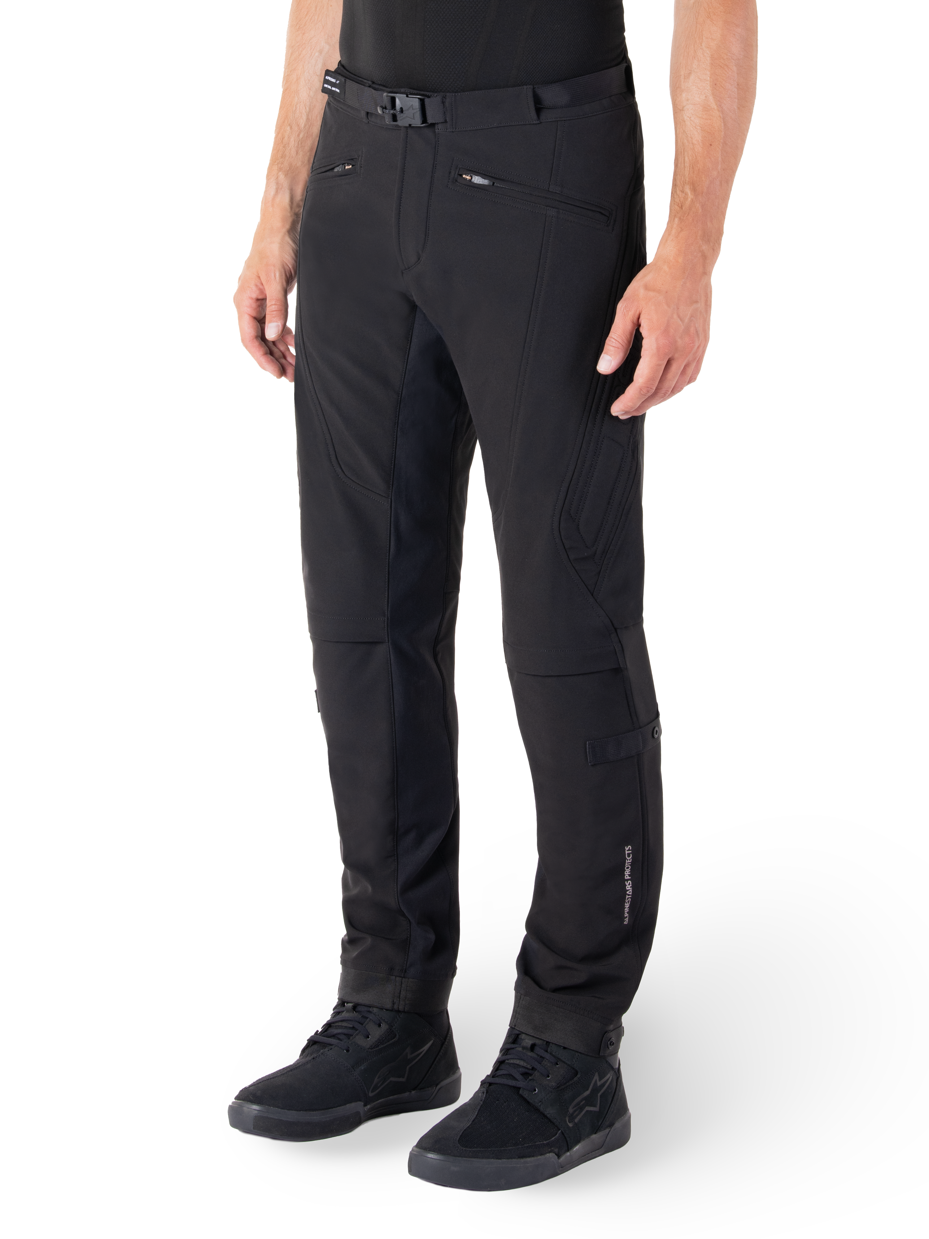 Alpinestars Alden Pants, miejskie spodnie motocyklowe, czarne, techniczna tkanina softshell o regularnym kroju, magnetyczna klamra w pasie, pikowane panele boczne, kieszenie na zamek i subtelne logo na dolnej części nogawki, noszone z czarnymi butami motocyklowymi