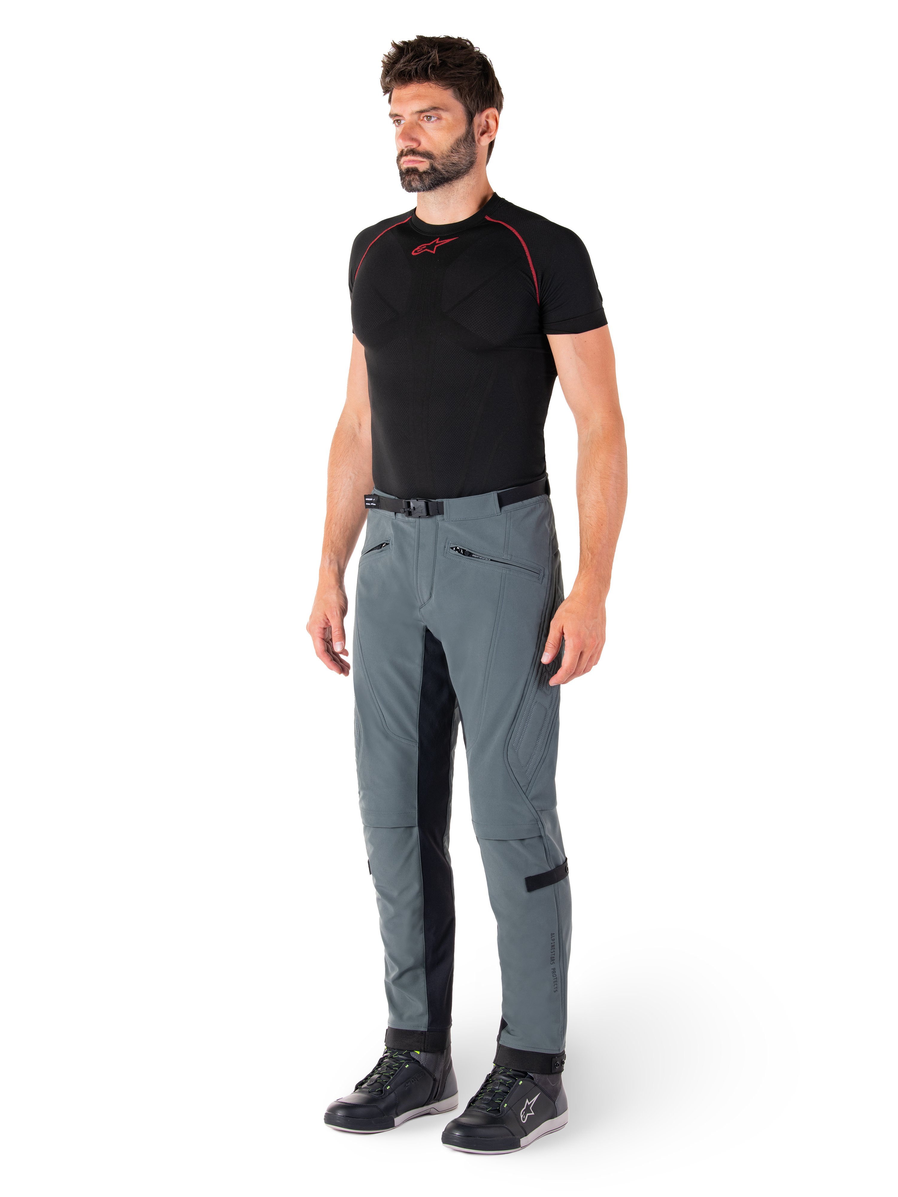 Spodnie Alpinestars Alden, techniczne spodnie motocyklowe w kolorze Urban Gray, wyposażone w pikowane panele boczne i czarny elastyczny materiał po wewnętrznej stronie nogawek, zestawione z czarną warstwą bazową i butami motocyklowymi, miejska odzież motocyklowa inspirowana streetwearem