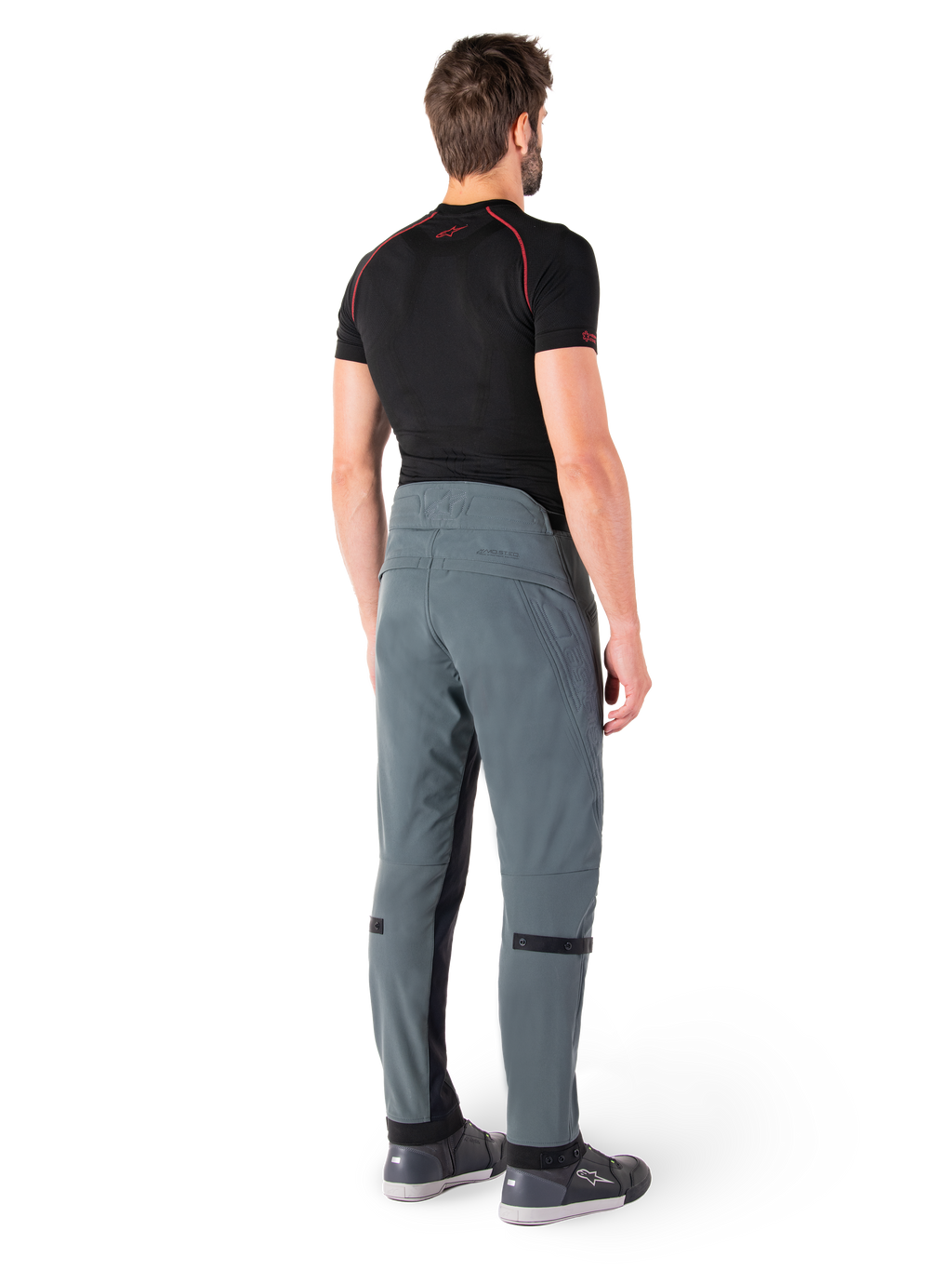 Spodnie Alpinestars Alden, Urban Gray, widok z tyłu, techniczne tekstylne spodnie motocyklowe z pikowanymi detalami w górnej części talii z tyłu i na nogawkach, w zestawieniu z czarną warstwą bazową i szarymi butami do jazdy, współczesny miejski styl streetwearowy.