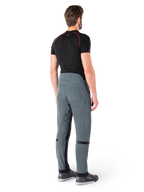 Spodnie Alpinestars Alden, Urban Gray, widok z tyłu, techniczne tekstylne spodnie motocyklowe z pikowanymi detalami w górnej części talii z tyłu i na nogawkach, w zestawieniu z czarną warstwą bazową i szarymi butami do jazdy, współczesny miejski styl streetwearowy.