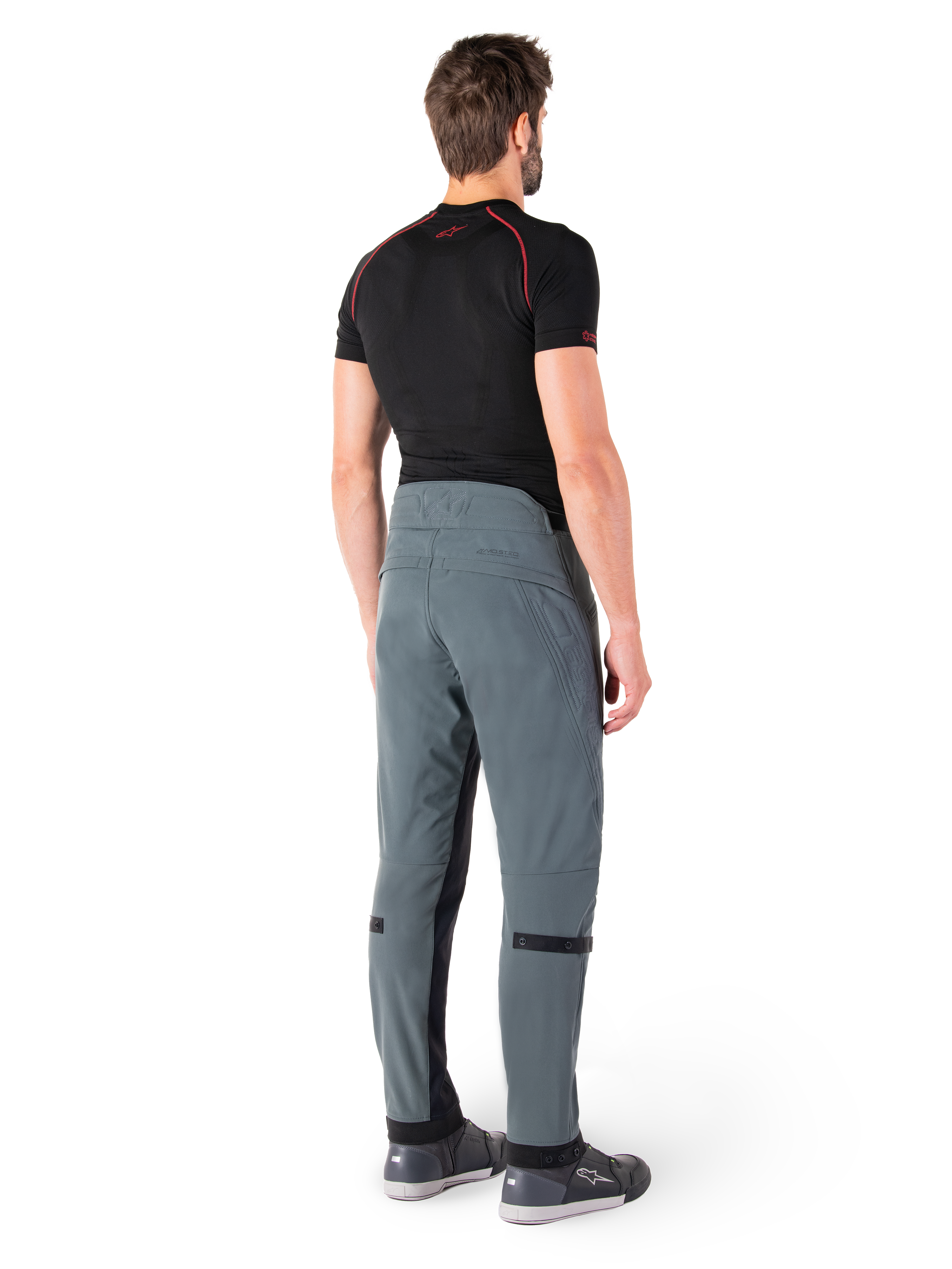 Spodnie Alpinestars Alden, Urban Gray, widok z tyłu, techniczne tekstylne spodnie motocyklowe z pikowanymi detalami w górnej części talii z tyłu i na nogawkach, w zestawieniu z czarną warstwą bazową i szarymi butami do jazdy, współczesny miejski styl streetwearowy.