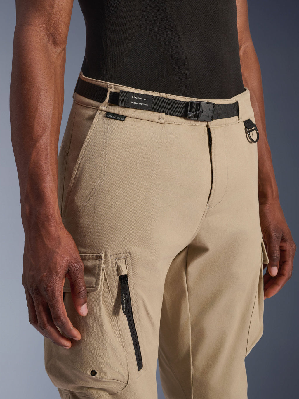 Alpinestars Flex-AST Cargo Pants, motocyklowe spodnie cargo, jasnobeżowe, ze zintegrowanym czarnym paskiem z logo, metalowym pierścieniem D-ring, boczną kieszenią na zamek i wytrzymałą tkaniną twill, zapewniające miejski styl użytkowy