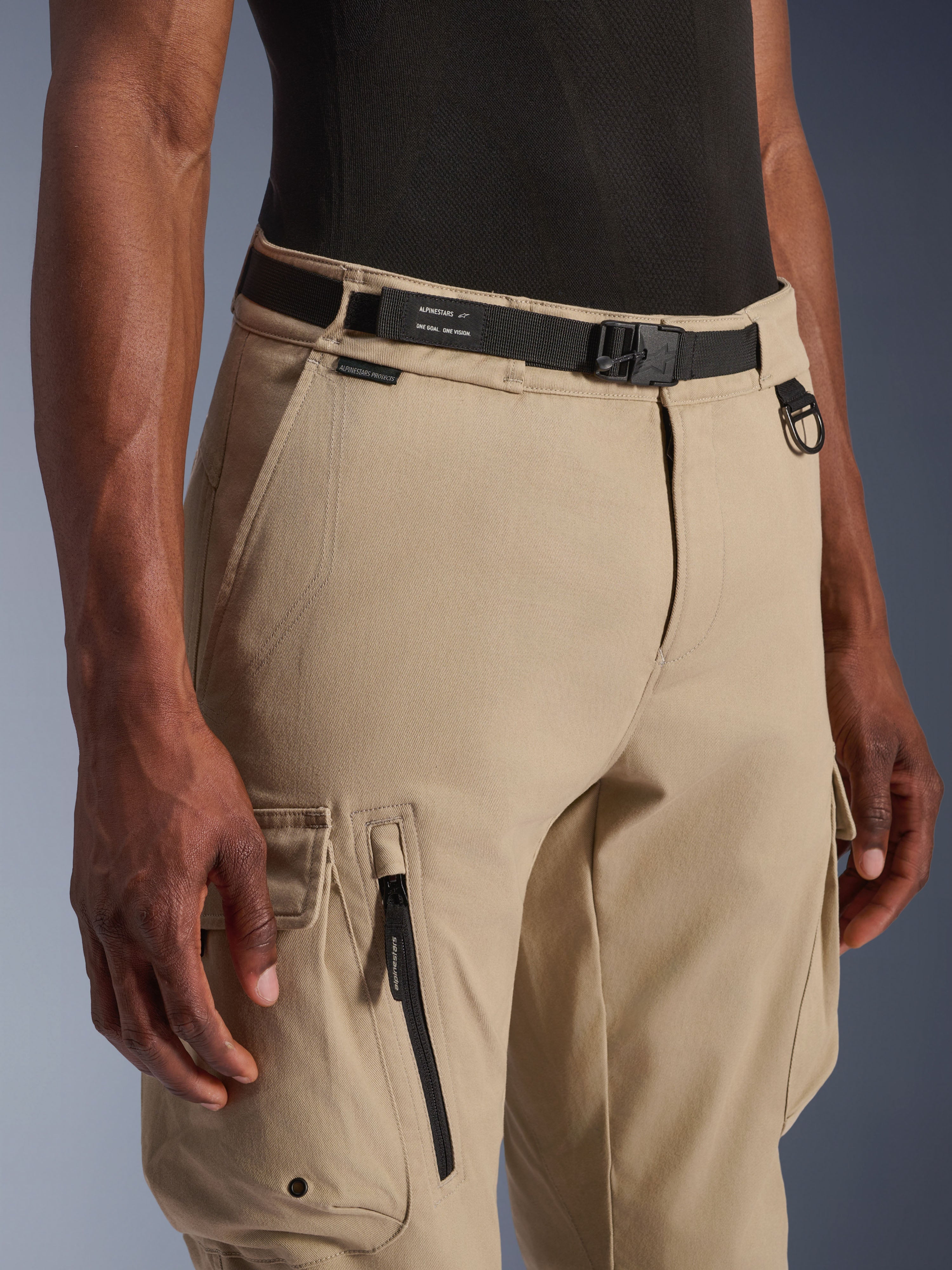 Alpinestars Flex-AST Cargo Pants, motocyklowe spodnie cargo, jasnobeżowe, ze zintegrowanym czarnym paskiem z logo, metalowym pierścieniem D-ring, boczną kieszenią na zamek i wytrzymałą tkaniną twill, zapewniające miejski styl użytkowy