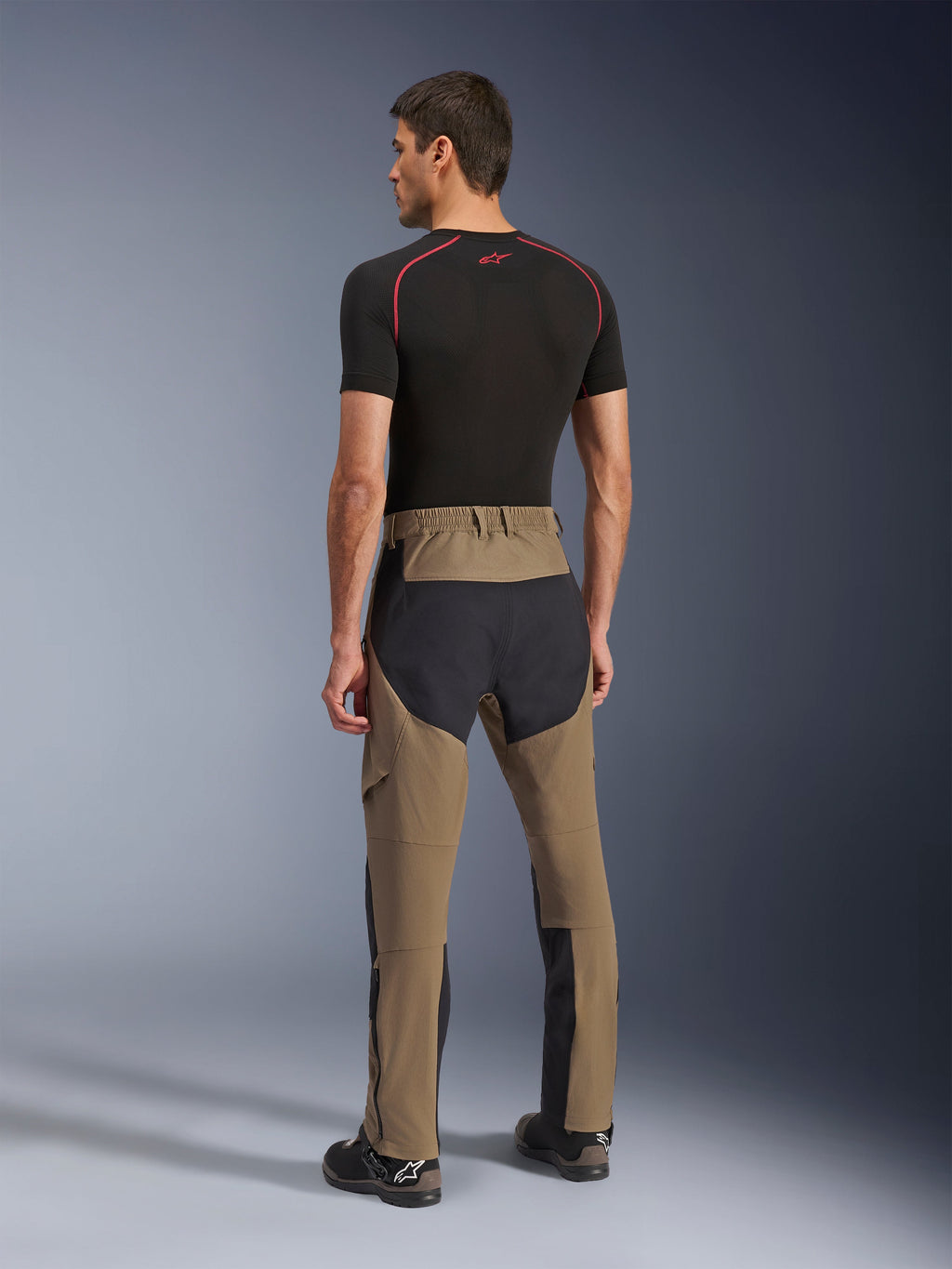 Alpinestars Flex-AST Explorer Pants, motocyklowe spodnie adventure, Walnut Black, widok z tyłu na modelu pokazujący czarne panele ripstop na siedzeniu i nogawkach, elastyczna konstrukcja tekstylna oraz długie zamki u dołu nogawek do adventure touring