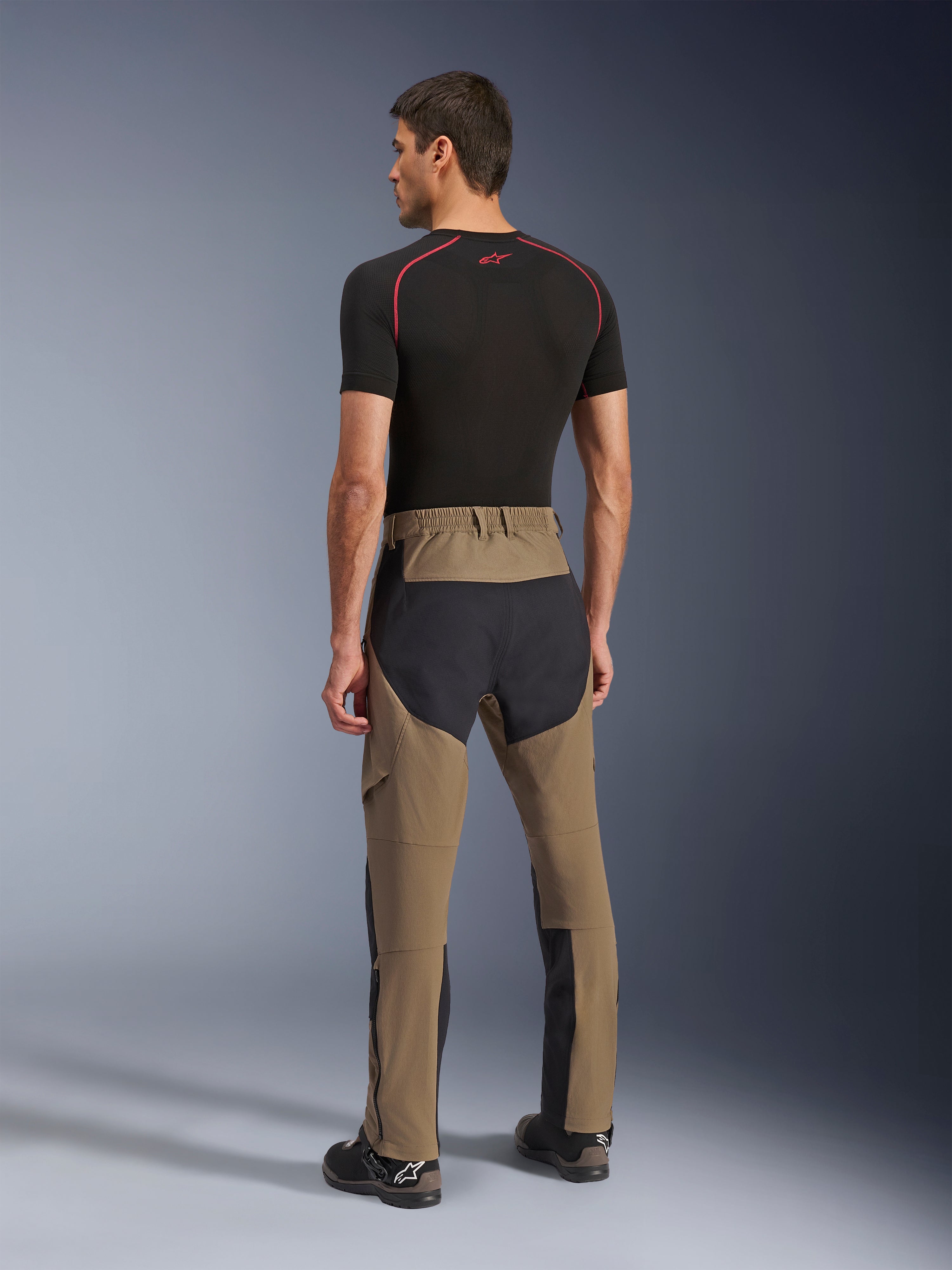 Alpinestars Flex-AST Explorer Pants, motocyklowe spodnie adventure, Walnut Black, widok z tyłu na modelu pokazujący czarne panele ripstop na siedzeniu i nogawkach, elastyczna konstrukcja tekstylna oraz długie zamki u dołu nogawek do adventure touring