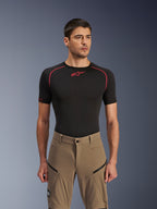 Alpinestars Flex-AST Explorer Pants, spodnie motocyklowe adventure, kolor Walnut Black, prezentowane przez modela w czarnej koszulce termoaktywnej, z ukośnymi kieszeniami cargo na zamek i wytrzymałą, elastyczną konstrukcją tekstylną.