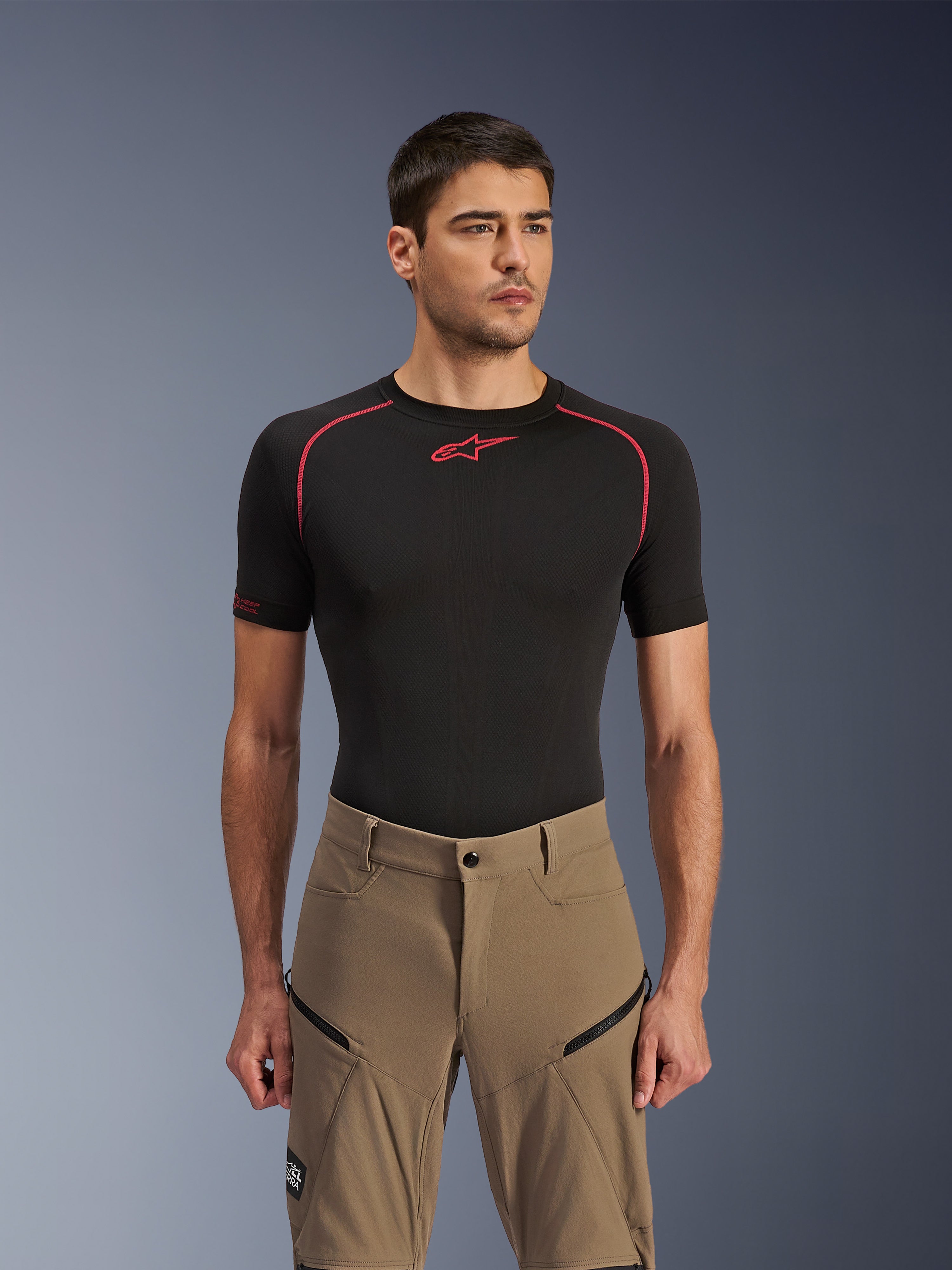 Alpinestars Flex-AST Explorer Pants, spodnie motocyklowe adventure, kolor Walnut Black, prezentowane przez modela w czarnej koszulce termoaktywnej, z ukośnymi kieszeniami cargo na zamek i wytrzymałą, elastyczną konstrukcją tekstylną.