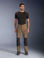 Alpinestars Flex-AST Explorer Pants, spodnie motocyklowe turystyczne, orzechowy brąz i czarny, ze wzmocnionymi panelami na kolanach i kieszeniami na udach zapinanymi na zamek, noszone z czarną warstwą bazową z krótkim rękawem, widok na całą sylwetkę