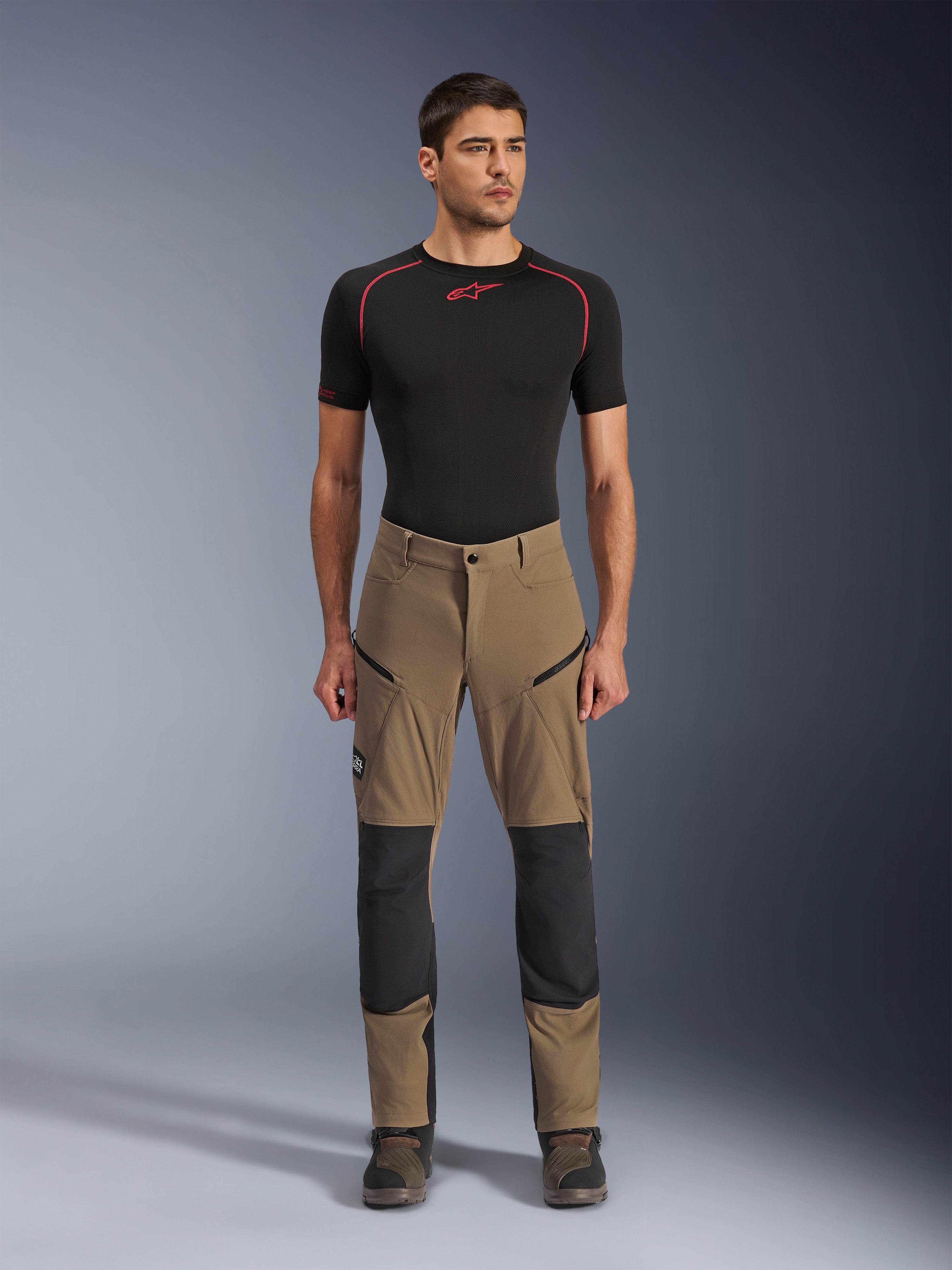Alpinestars Flex-AST Explorer Pants, spodnie motocyklowe turystyczne, orzechowy brąz i czarny, ze wzmocnionymi panelami na kolanach i kieszeniami na udach zapinanymi na zamek, noszone z czarną warstwą bazową z krótkim rękawem, widok na całą sylwetkę
