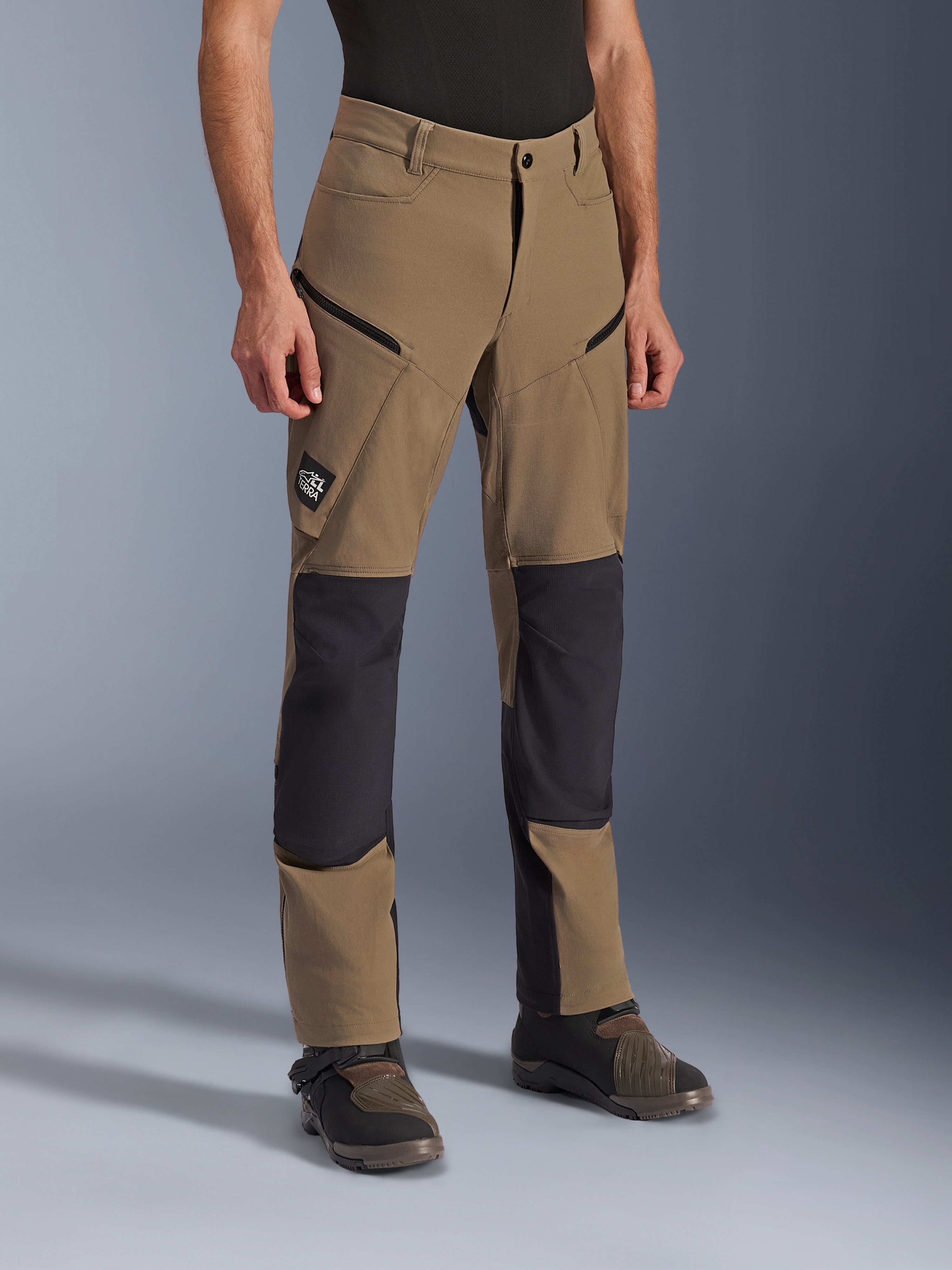 Spodnie Alpinestars Flex-AST Explorer, motocyklowe spodnie adventure w kolorze Walnut Black, beżowa tkanina z czarnymi wzmocnionymi panelami na kolanach i siedzeniu, kieszenie cargo na zamek, naszywka z logo All Terra, widoczne w zestawieniu z technicznymi butami motocyklowymi