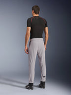 Widok z tyłu modelu ubranego w spodnie Alpinestars Aeroshell Airflow w kolorze Mid Gray, zestawione z czarną koszulką termoaktywną i czarnymi butami, podkreślający laserowo perforowane strefy na łydkach oraz sportowy krój.