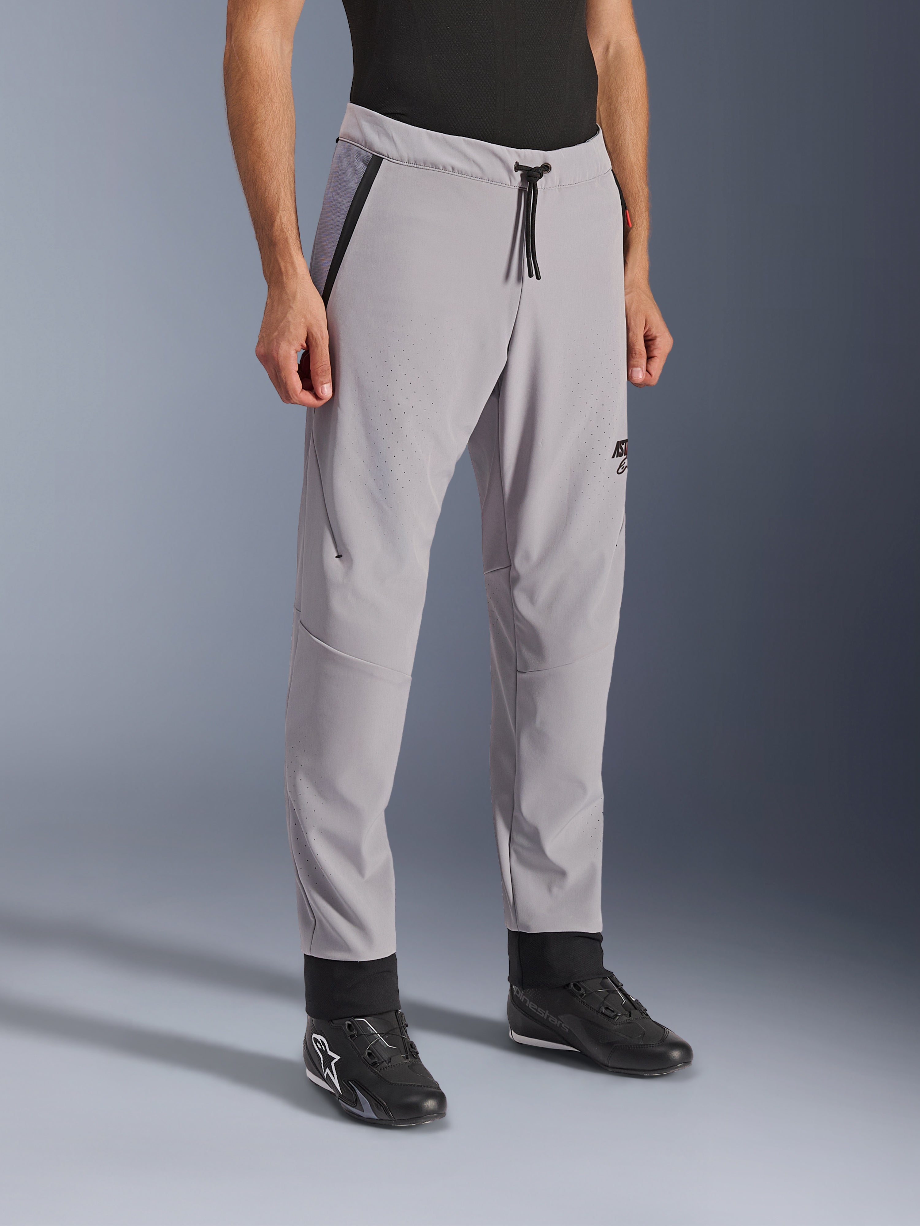 Alpinestars Aeroshell Airflow Pants, Mid Gray, lekkie spodnie motocyklowe z laserowo perforowanymi strefami wentylacyjnymi na udach i goleniach, z elastycznym pasem regulowanym sznurkiem i dopasowanym sportowym krojem, zaprezentowane na modelu w czarnych butach motocyklowych.
