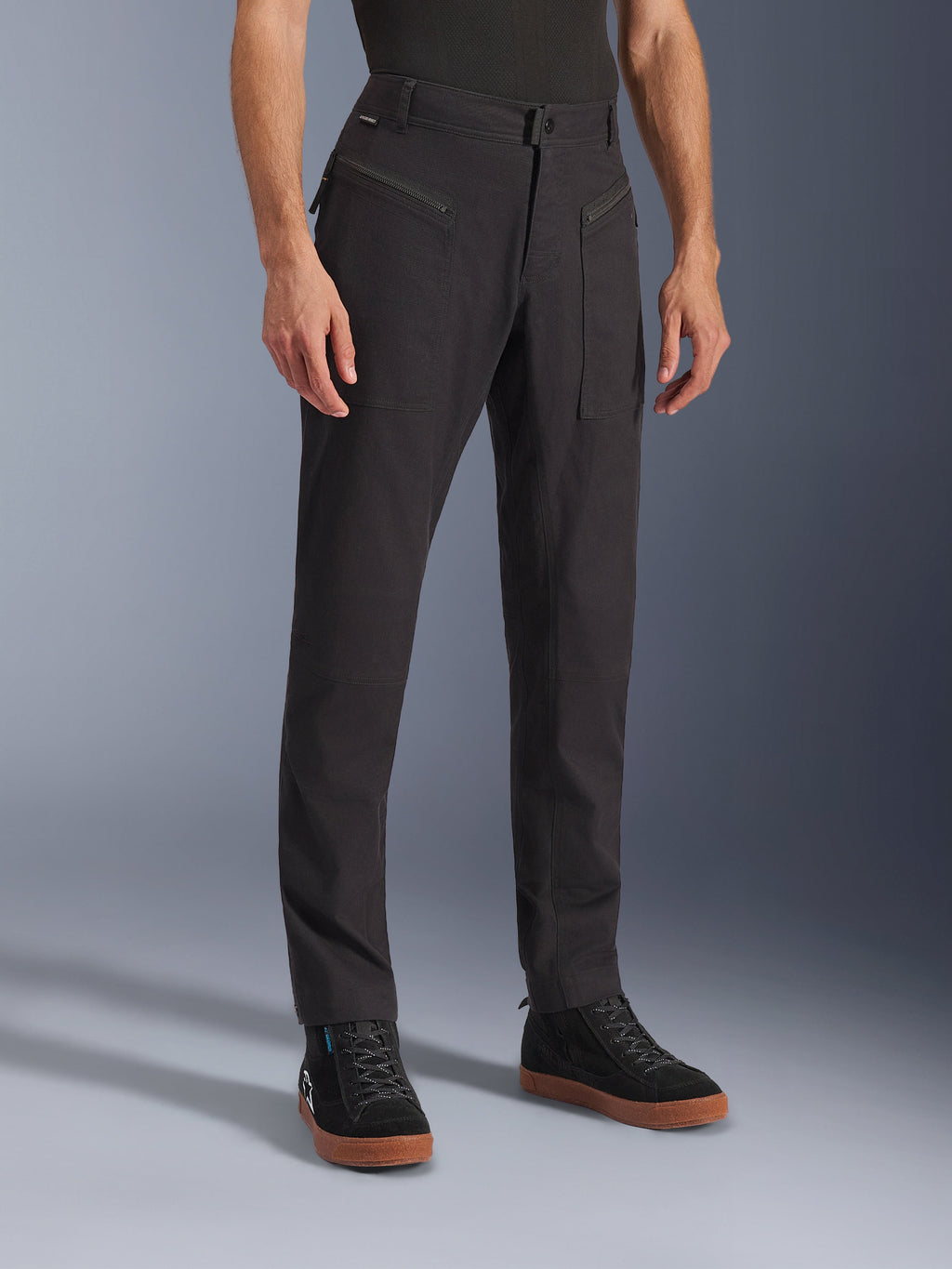 Spodnie Alpinestars Flex-AST Canvas, czarne, miejskie spodnie motocyklowe, prezentowane na modelu w czarnych sneakersach, tradycyjny design odzieży roboczej, elastyczna tkanina polibawełniana, funkcjonalne przednie kieszenie zapinane na zamek.