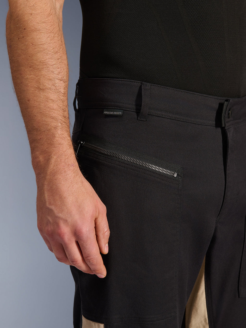Alpinestars Flex-AST Canvas Pants w kolorze Black Aluminum, zbliżenie na okolicę biodra z poziomą kieszenią zapinaną na zamek, szlufkami i małą metką z marką, wytrzymała konstrukcja z elastycznej polibawełny do jazdy miejskiej.