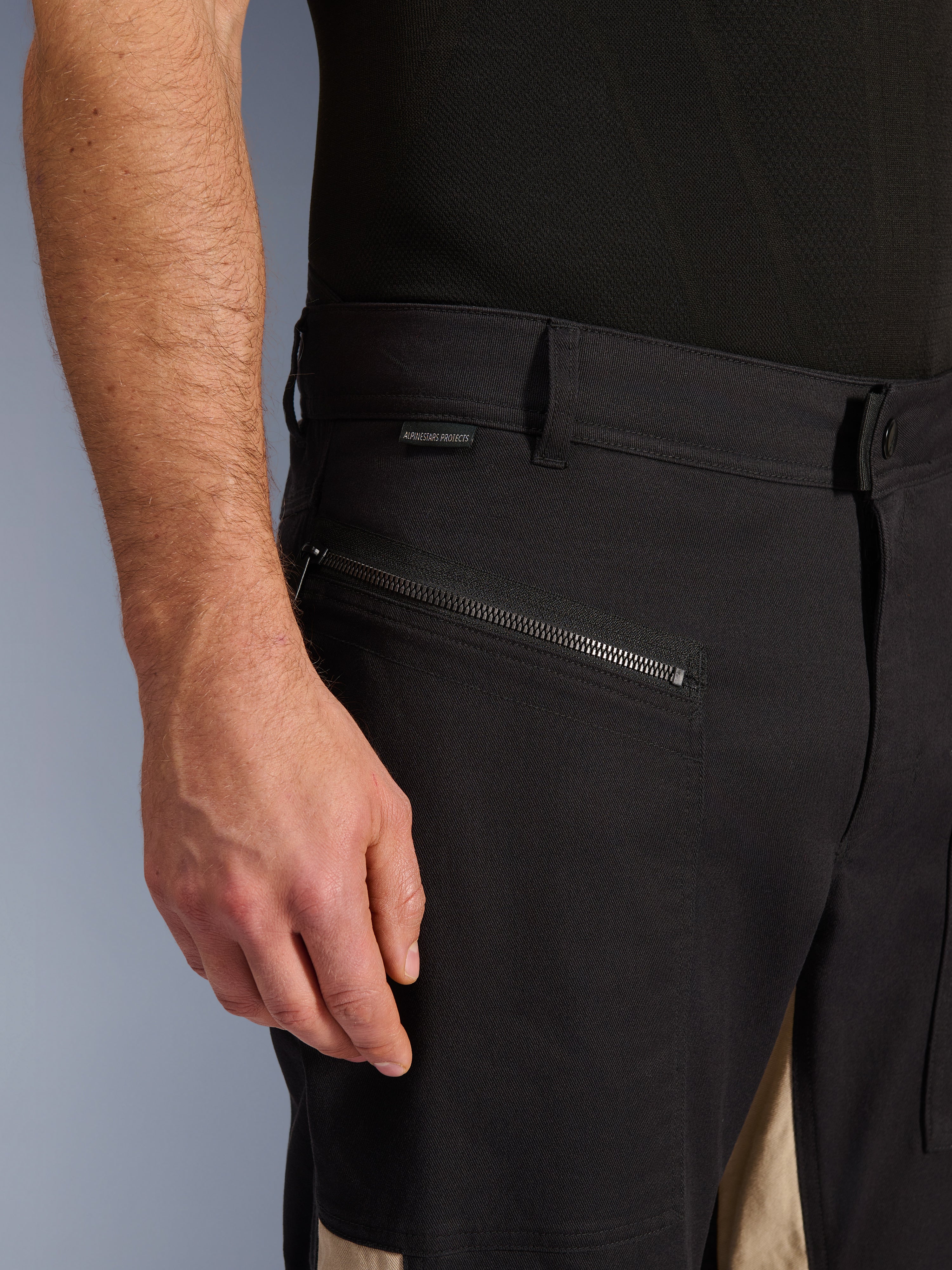 Alpinestars Flex-AST Canvas Pants w kolorze Black Aluminum, zbliżenie na okolicę biodra z poziomą kieszenią zapinaną na zamek, szlufkami i małą metką z marką, wytrzymała konstrukcja z elastycznej polibawełny do jazdy miejskiej.