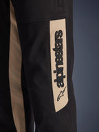 Spodnie Alpinestars Flex-AST Canvas, zbliżenie na detal boku nogawki, czarne z beżowym panelem akcentującym Aluminum, pionowe czarne logo Alpinestars i ikona gwiazdy, wytrzymały twill z polibawełny do miejskiej jazdy motocyklowej