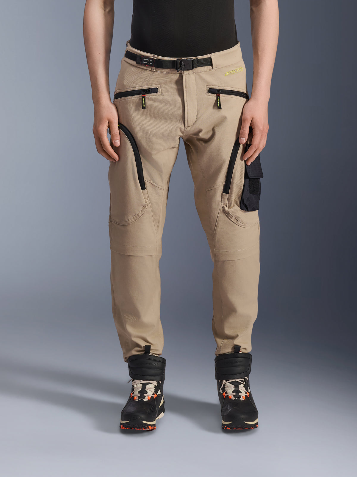 Spodnie Alpinestars Acteon, miejskie spodnie motocyklowe, piaskowy beż, wielokieszeniowy design cargo z czarnymi odwróconymi zamkami, zintegrowany pasek w talii i zwężany krój, w zestawie z czarno-pomarańczowymi butami