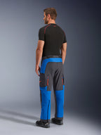 Alpinestars Maxdura Dual Pants, spodnie motocyklowe adventure, niebieskie i ciemnoszare, widok z tyłu na modelu, pomarańczowe otwory wentylacyjne na zamek, krój adventure na buty, wytrzymały, elastyczny materiał