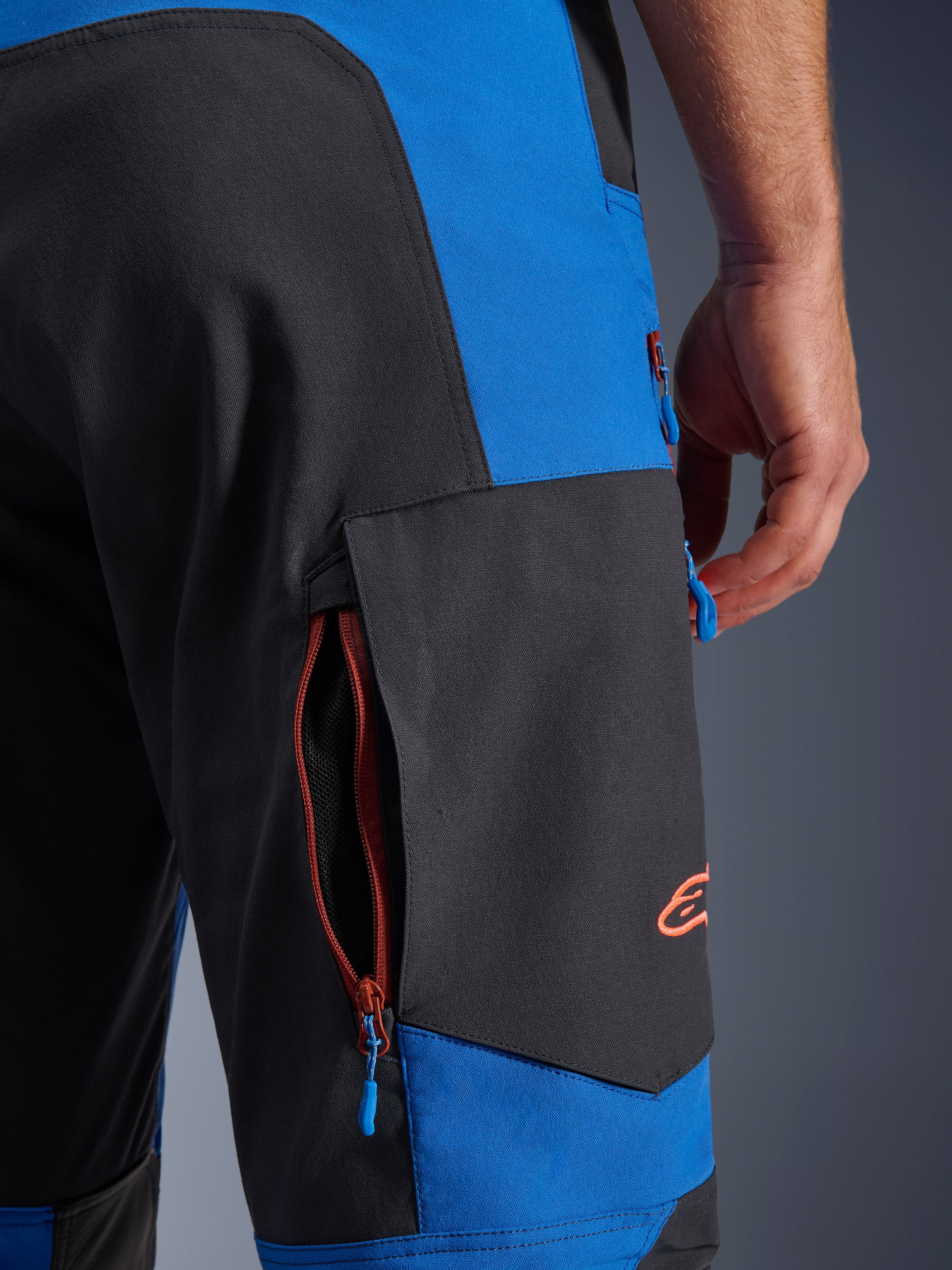 Spodnie Alpinestars Maxdura Dual, Royal Blue i Deep Gray, zbliżenie na boczną kieszeń cargo zapinaną na zamek, niebieskie uchwyty zamków, pomarańczowe haftowane logo, odzież motocyklowa adventure