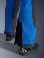 Spodnie Alpinestars Maxdura Dual, kolor niebieski Royal Blue i ciemnoszary Deep Gray, zbliżenie na regulowaną dolną część nogawki z zapięciami na zatrzaski i klinem, krój adventure typu over-the-boot, noszone z czarnymi butami motocyklowymi Alpinestars