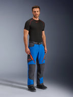 Alpinestars Maxdura Dual Pants, spodnie motocyklowe adventure, niebieskie i ciemnoszare z pomarańczowymi akcentami przy zamkach i logo, prezentowane przez modela w czarnej warstwie bazowej i butach, techniczny design ze wzmocnionymi panelami do jazdy dual-sport