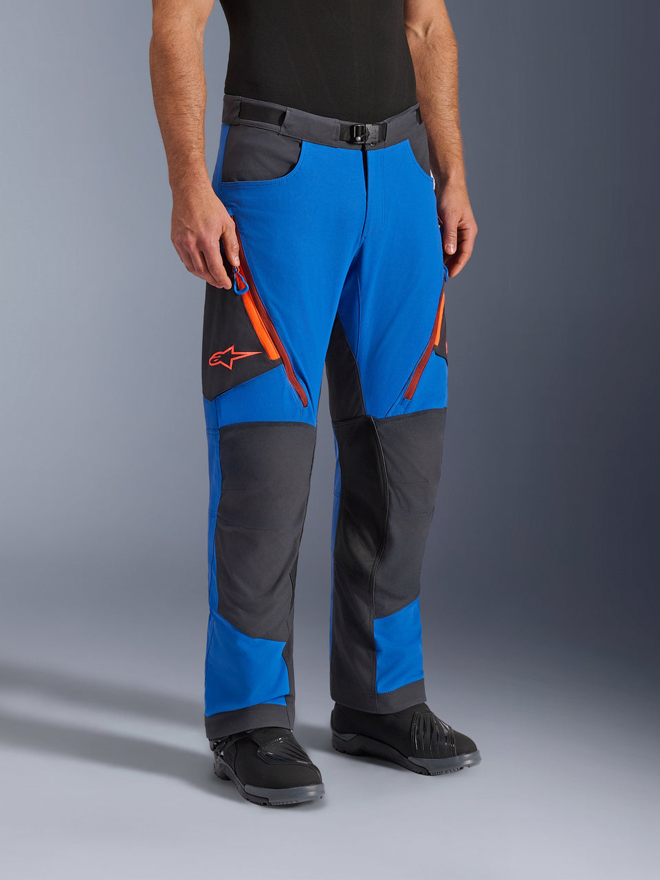 Alpinestars Maxdura Dual Pants, motocyklowe spodnie adventure, kolor Royal Blue i Deep Gray z pomarańczowymi akcentami, z wentylacyjnymi zamkami na udach, wzmocnionymi panelami na kolanach i paskiem z klamrą magnetyczną, techniczny krój na buty do jazdy dual-sport.