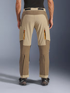 Alpinestars Maxdura Dual Pants, Walnut Aluminum, rear view of adventure motorcycle pants featuring tan and earth-tone panels, orange-zipped exhaust vents, and over-the-boot design, worn with black Alpinestars boots.