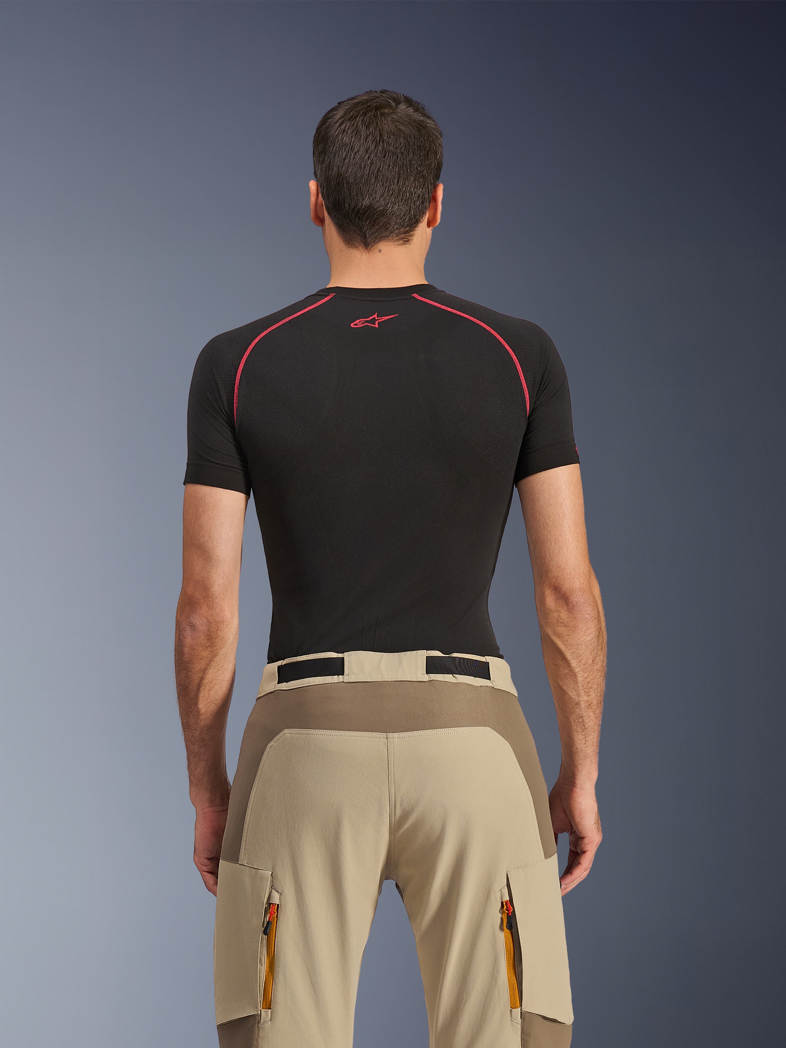 Alpinestars Maxdura Dual Pants, Adventure Motorcycle Pants, Walnut Aluminum, rear view showing reinforced seat panel and beige stretch fabric, zippered cargo pockets with orange pulls, worn with a black Alpinestars base layer shirt.
