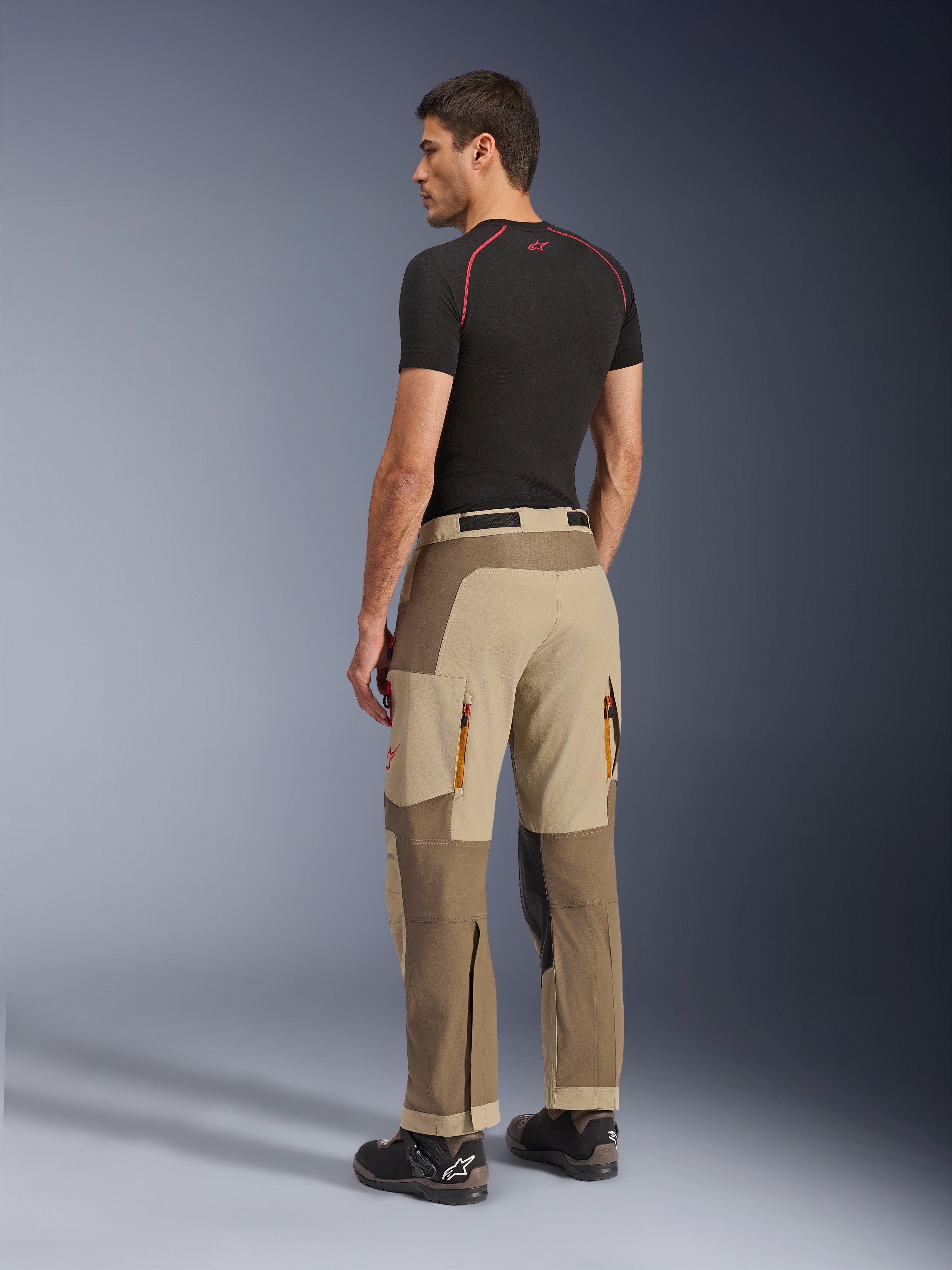 Alpinestars Maxdura Dual Pants, Adventure and Dual-Sport Riding Pants, Walnut Aluminum, rear view worn by a model with a black base layer and riding boots, featuring multi-panel construction with zippered rear vents and reinforced overlays.