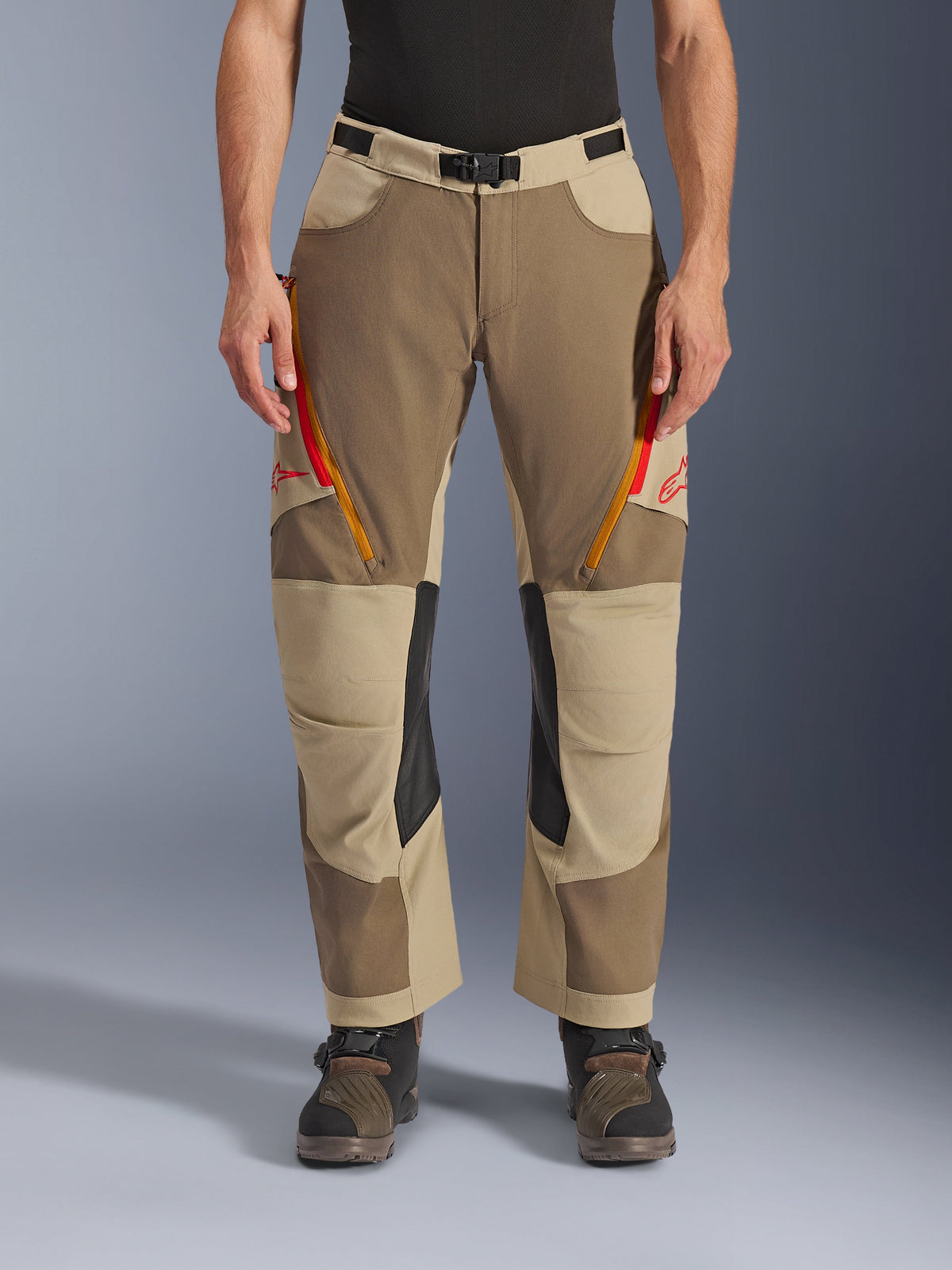 Alpinestars Maxdura Dual Pants, kolor Walnut Aluminum, spodnie motocyklowe adventure z czerwonymi i pomarańczowymi otworami wentylacyjnymi na udach, czarne skórzane panele po wewnętrznej stronie kolan, noszone z czarną warstwą bazową i solidnymi butami, wytrzymała wielotonowa konstrukcja do jazdy dual-sport