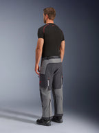 Spodnie Alpinestars Maxdura Dual, spodnie motocyklowe adventure, ciemnoszare i grafitowe, widoczne na modelu od tyłu z boku, czerwone akcenty na zamkach i logo, wzmocnione szare panele, kieszenie cargo, krój nakładany na buty