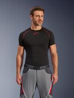 Alpinestars Maxdura Dual Pants, ciemnoszare i głęboko szare z czerwonymi akcentami, noszone z czarną koszulką termoaktywną z czerwonymi przeszyciami, sportowy krój ze zintegrowanym paskiem z magnetyczną klamrą, wytrzymała odzież motocyklowa adventure