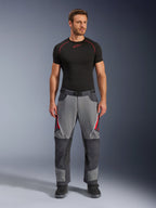 Spodnie motocyklowe Alpinestars Maxdura Dual, ciemnoszare i szare z czerwonymi akcentami, widok z przodu na modelu w czarnej warstwie bazowej Alpinestars i czarnych butach, wzmocnione panele i zapinane na zamek otwory wentylacyjne na udach, odzież motocyklowa typu adventure