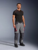 Alpinestars Maxdura Dual Pants, spodnie motocyklowe adventure, ciemnoszare i grafitowe, noszone z czarną warstwą bazową i butami, z czerwonymi otworami wentylacyjnymi na zamki, wzmocnionymi panelami na kolanach i siedzeniu oraz paskiem w talii, sportowy krój do jazdy dual-sport