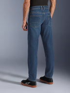 Alpinestars Flex-AST 5 Denim Pants, niebieskie Indigo Washed, widok z tyłu osoby ubranej w codzienne jeansy motocyklowe o zwężanym kroju, zestawione z czarnymi sneakersami Alpinestars, z tylnymi kieszeniami i wzmocnionymi szwami do jazdy miejskiej