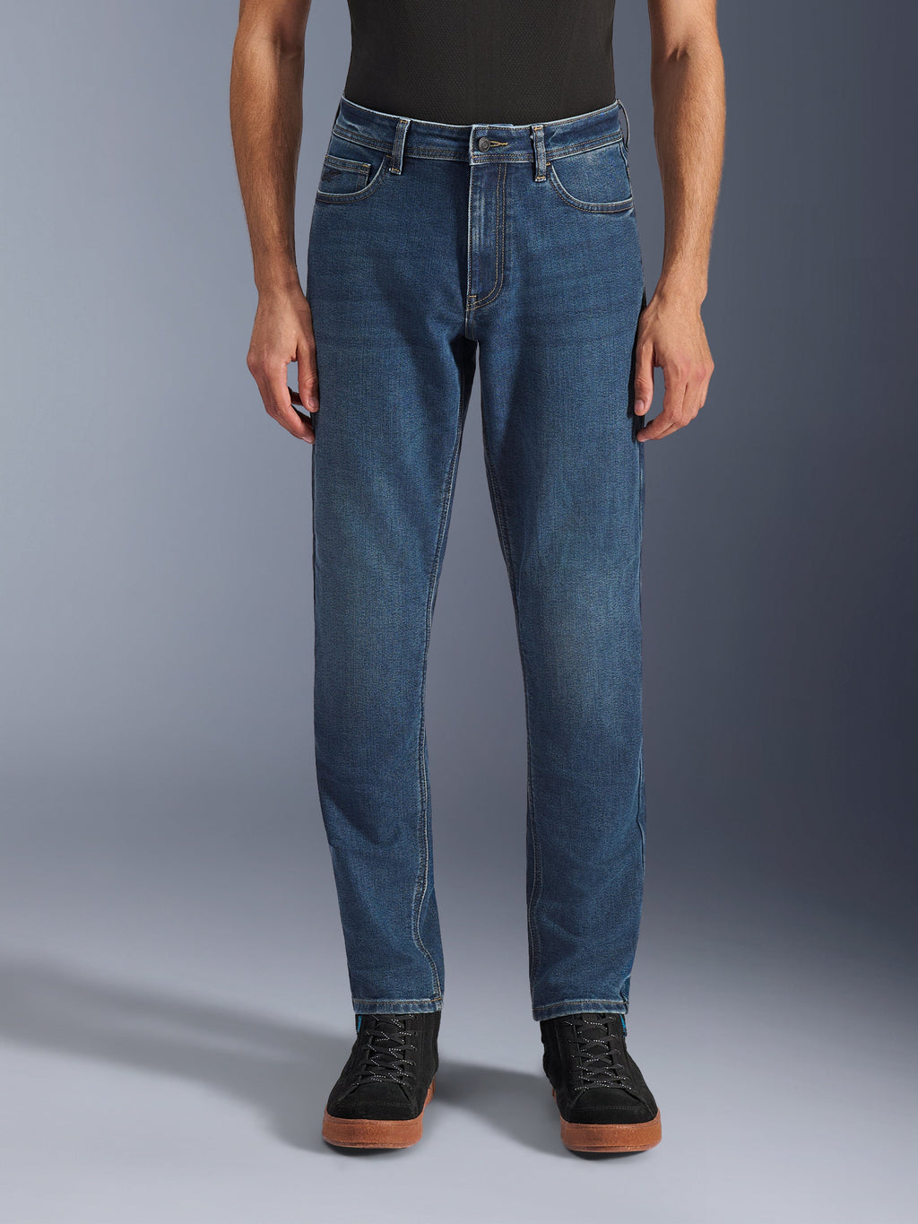 Alpinestars Flex-AST 5 Denim Pants, miejskie dżinsy motocyklowe, Indigo Washed Blue, widok z przodu prezentujący nowoczesny, zwężany krój i klasyczny fason z pięcioma kieszeniami, noszone z czarną koszulką i sneakersami, zaprojektowane z myślą o komforcie i ochronie podczas jazdy miejskiej.