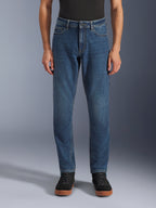 Alpinestars Flex-AST 5 Denim Pants, miejskie dżinsy motocyklowe, Indigo Washed Blue, widok z przodu prezentujący nowoczesny, zwężany krój i klasyczny fason z pięcioma kieszeniami, noszone z czarną koszulką i sneakersami, zaprojektowane z myślą o komforcie i ochronie podczas jazdy miejskiej.