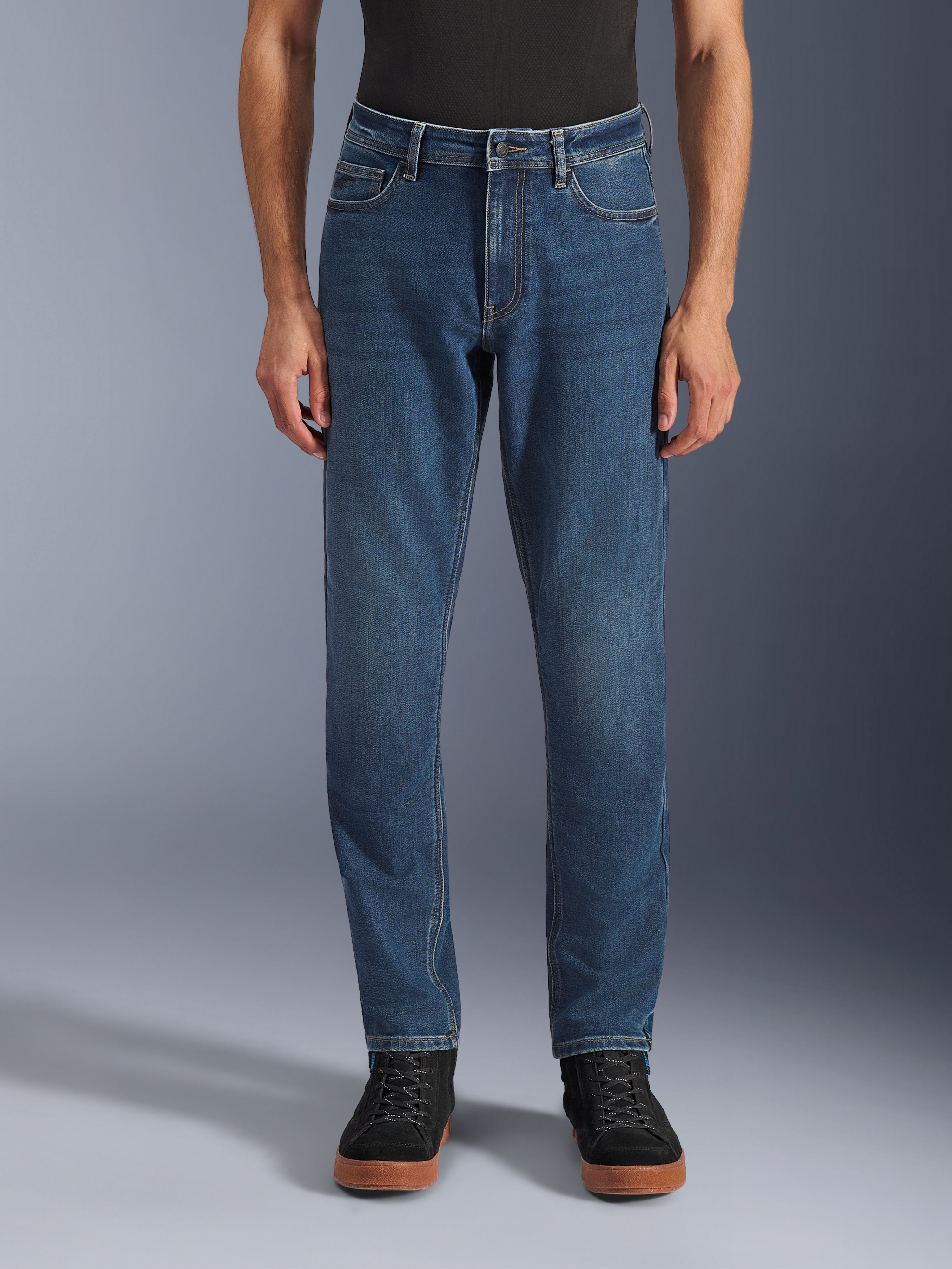 Alpinestars Flex-AST 5 Denim Pants, miejskie dżinsy motocyklowe, Indigo Washed Blue, widok z przodu prezentujący nowoczesny, zwężany krój i klasyczny fason z pięcioma kieszeniami, noszone z czarną koszulką i sneakersami, zaprojektowane z myślą o komforcie i ochronie podczas jazdy miejskiej.