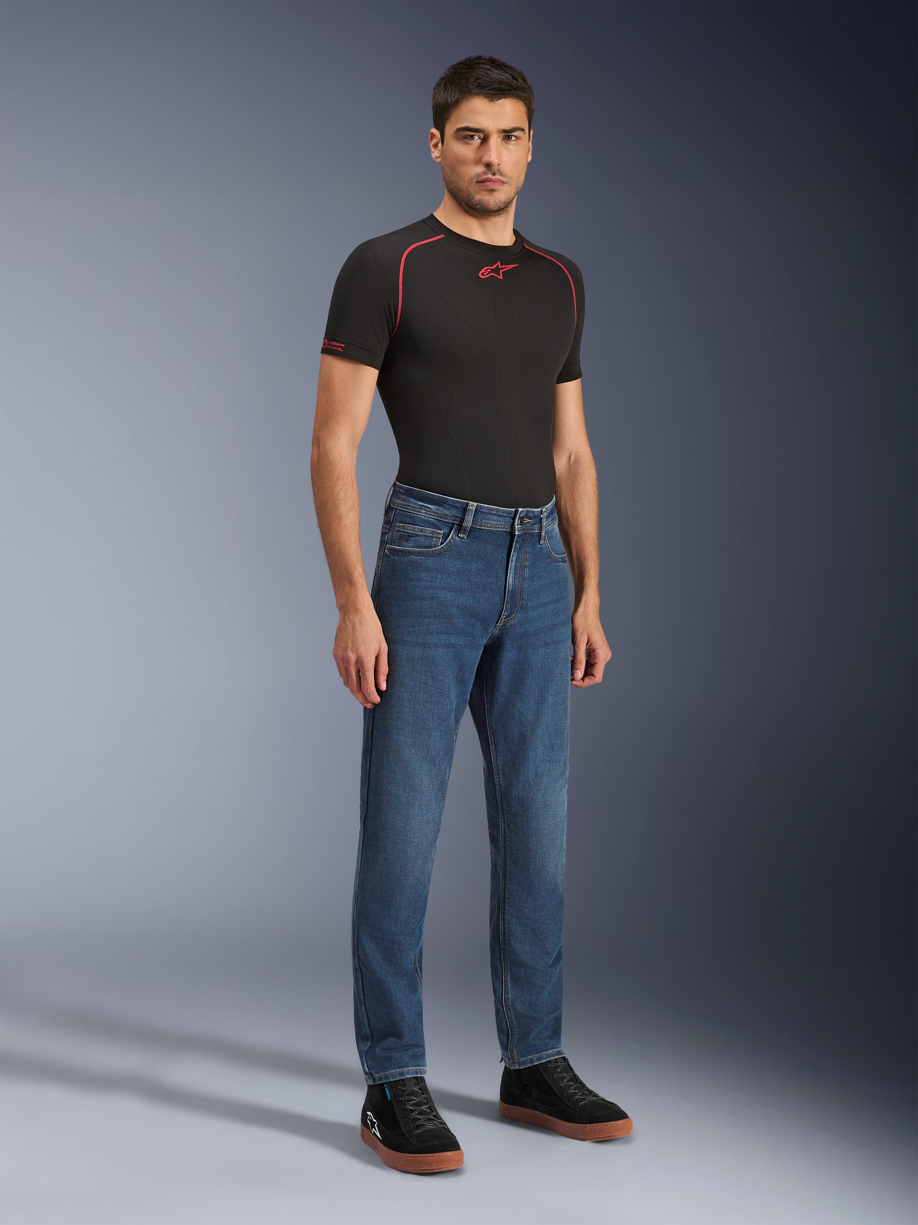 Spodnie Alpinestars Flex-AST 5 Denim, motocyklowe jeansy Indigo Washed, nowoczesny zwężany krój, męski model w czarnej koszulce technicznej i czarnych trampkach, codzienna miejska odzież motocyklowa.
