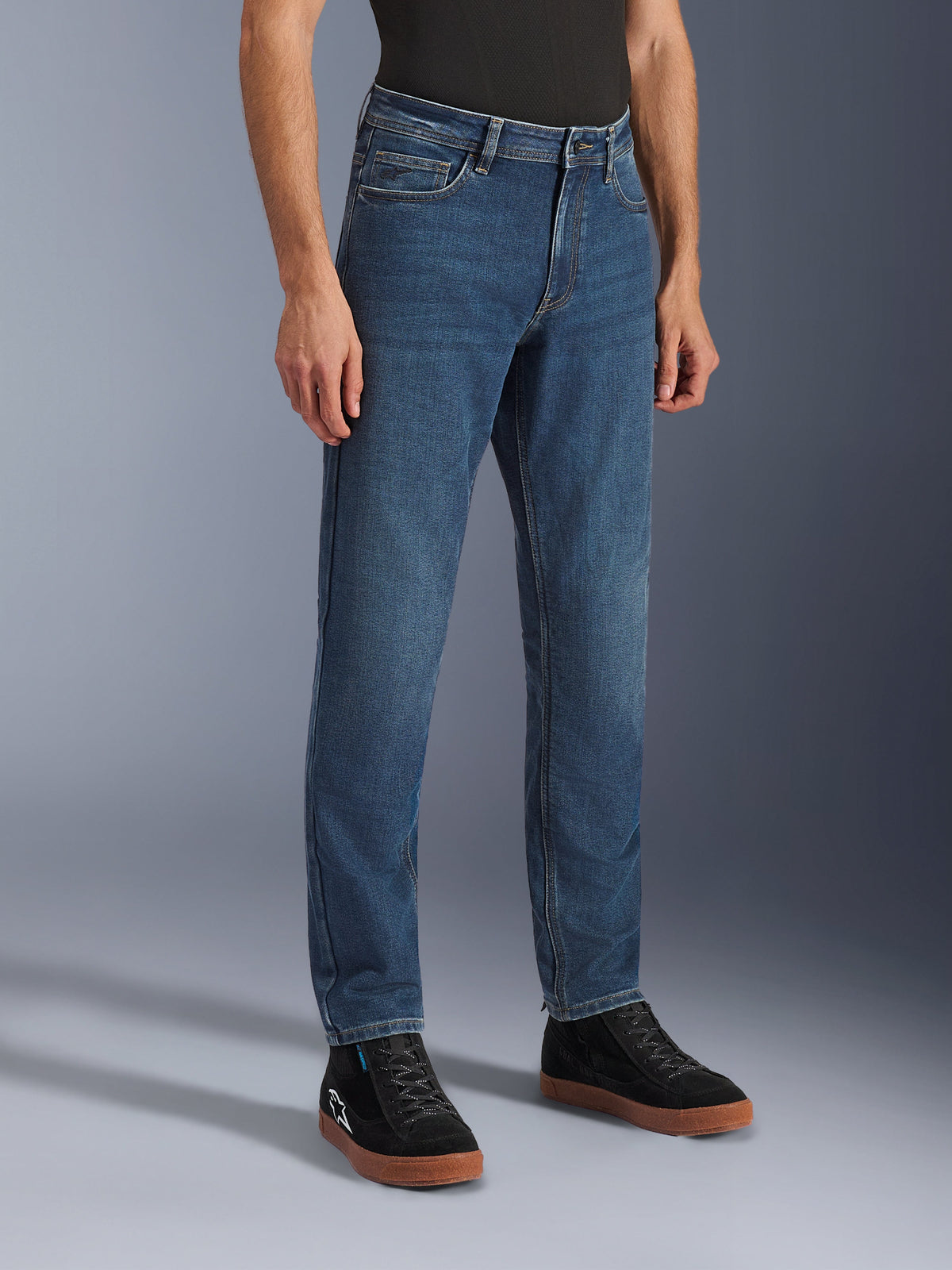 Spodnie Alpinestars Flex-AST 5 Denim, jeansy motocyklowe Indigo Washed, standardowy krój zwężany, zestawione z czarnymi wysokimi sneakersami i czarną koszulką, miejska odzież motocyklowa o klasycznym jeansowym wyglądzie