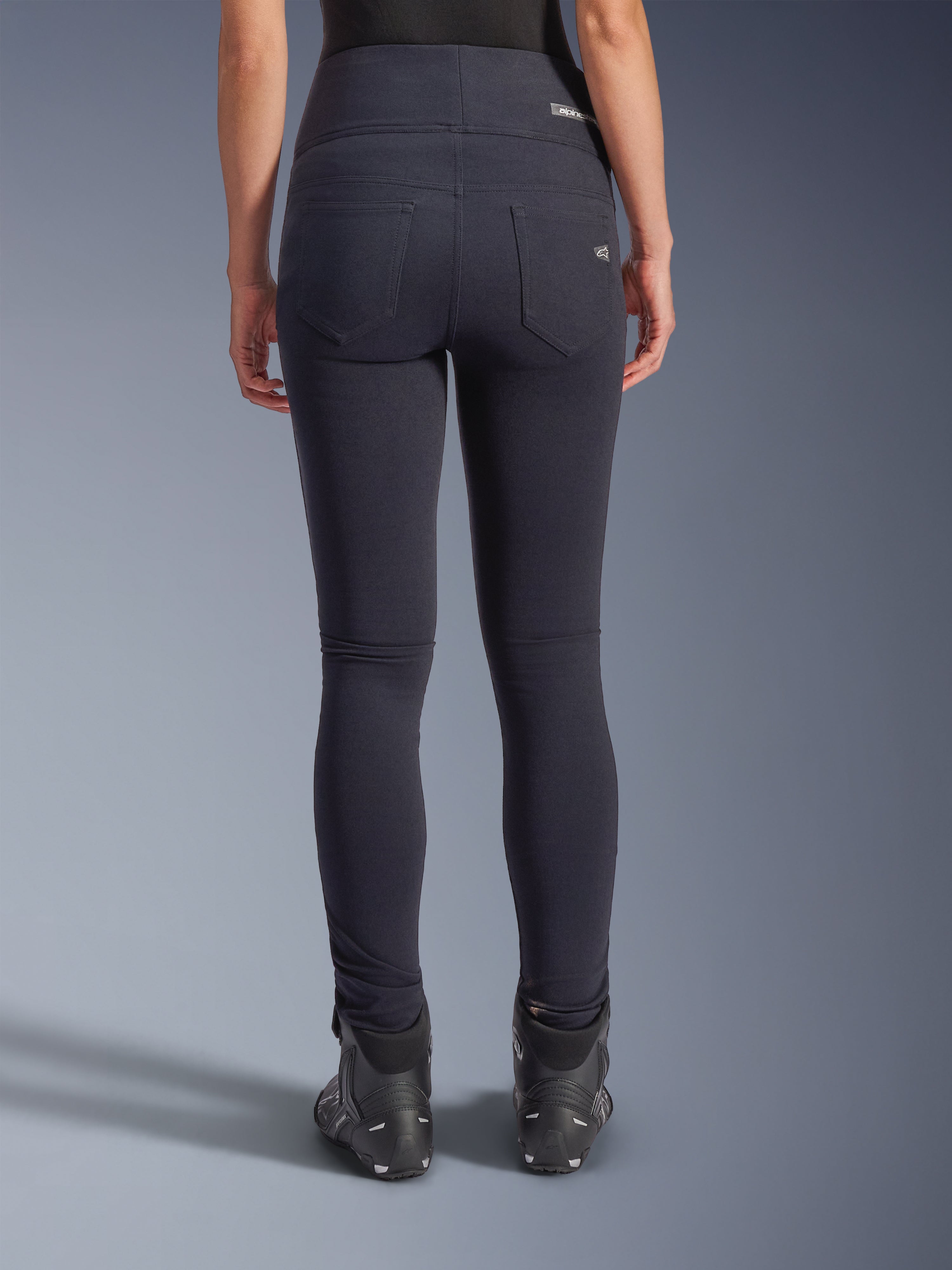 Legginsy Alpinestars Stella Flex-AST, miejskie spodnie motocyklowe, czarne, widok z tyłu prezentujący wysoki stan i dopasowany krój skinny, dwie funkcjonalne kieszenie tylne z subtelnym brandingiem, elastyczny materiał tekstylny, zestawione z czarnymi butami motocyklowymi